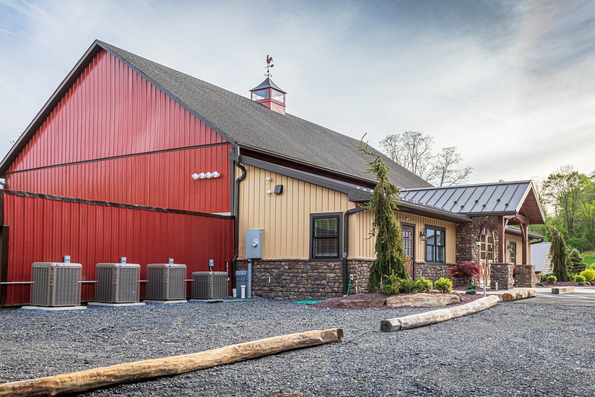 Red and tan barn-style building with a gravel driveway. Exterior includes stone, wood, and metal elements.