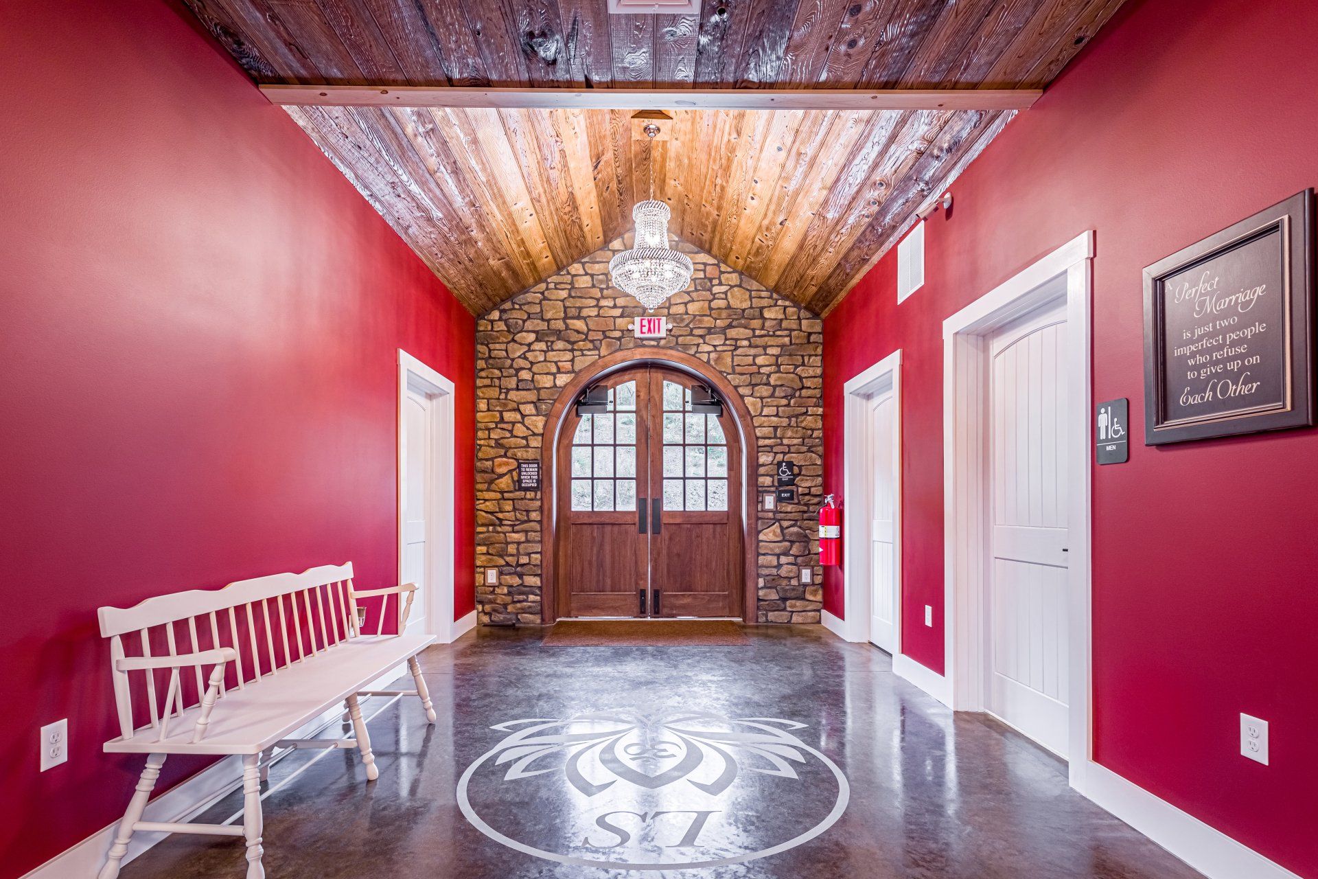 Hallway with stone archway doorway, red walls, wooden ceiling, white bench, and decorative floor inlay.