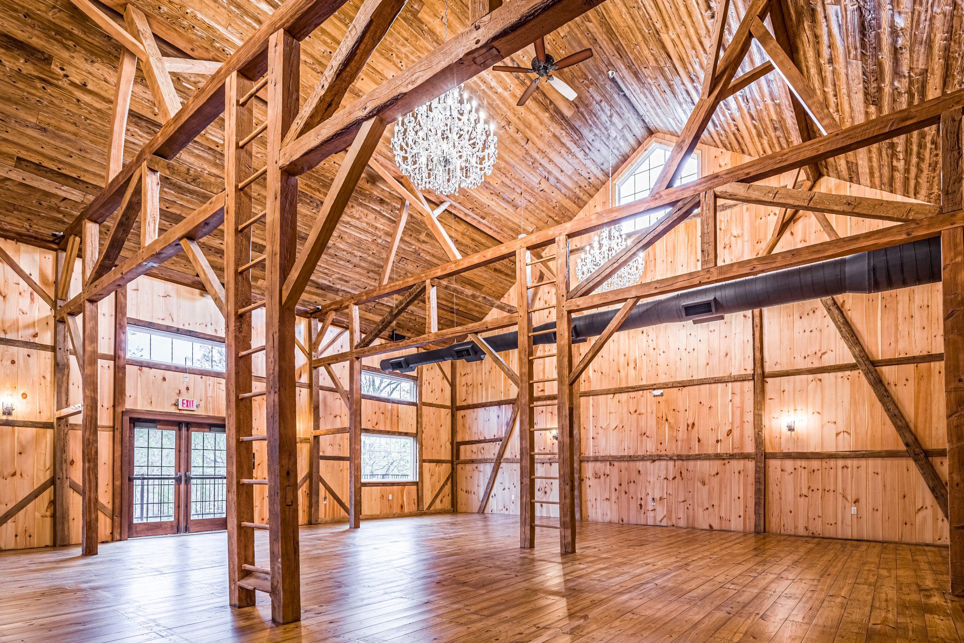 Wooden-beamed event space with wood walls and floor, a chandelier, and windows.