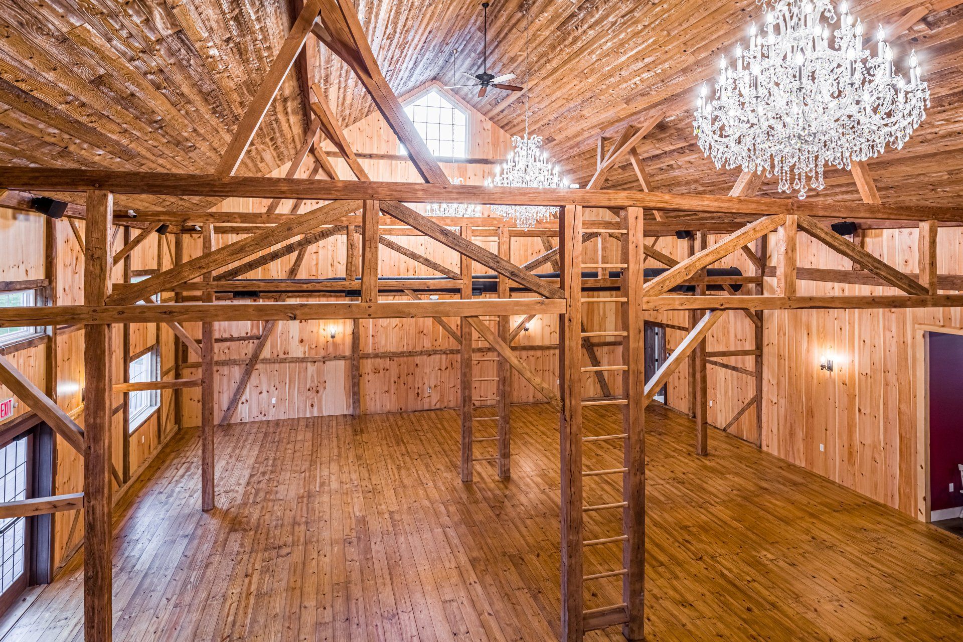Wooden barn interior with chandeliers, beams, and a loft.