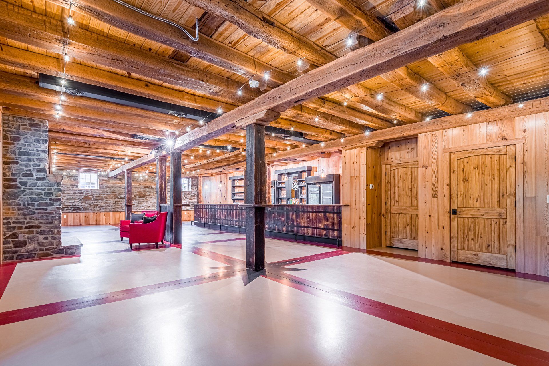 Spacious interior, wood-paneled walls and ceiling, exposed beams, red and white floor, seating area.