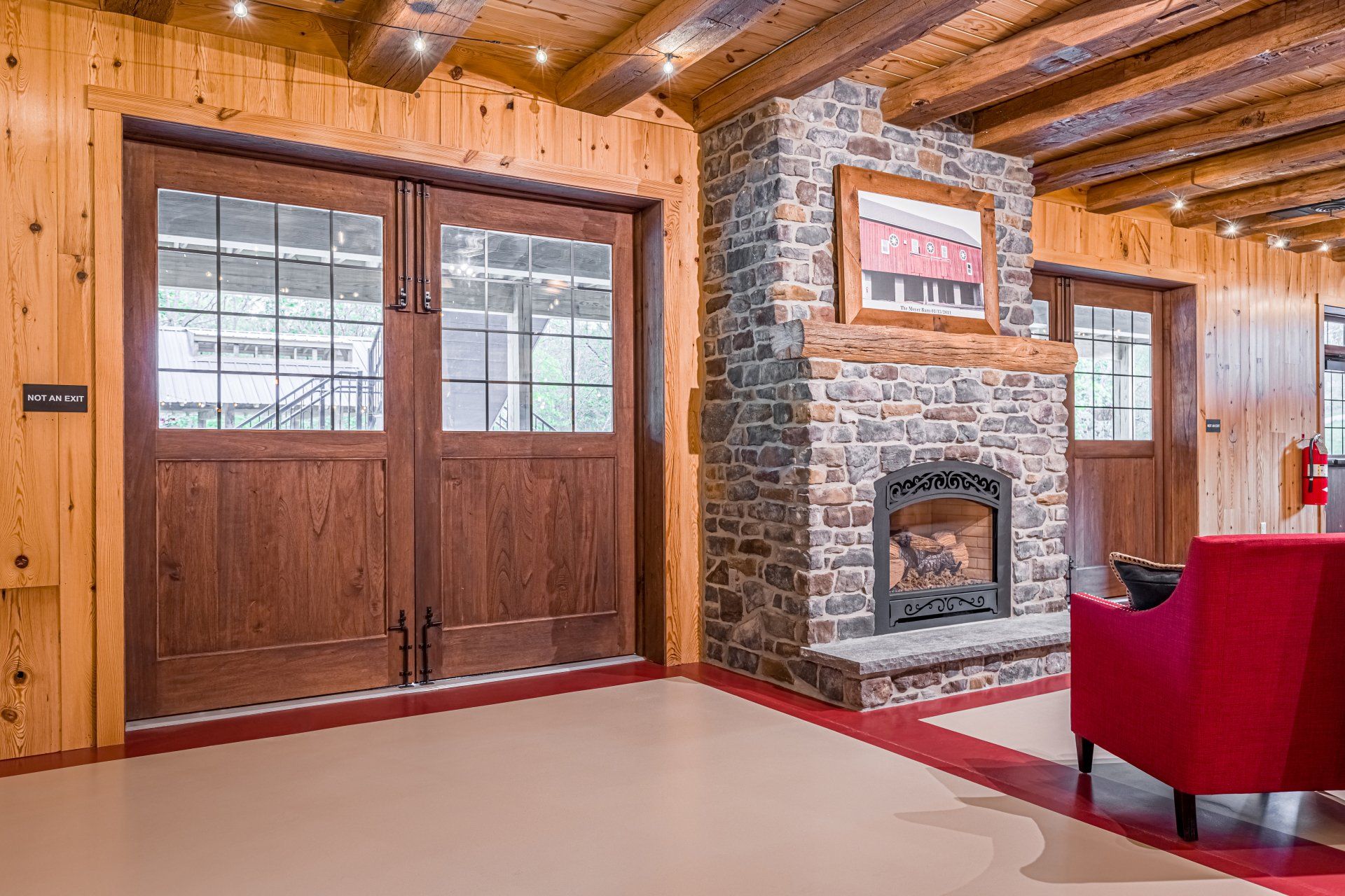 Wooden paneled room with fireplace, doors, red chair, and exposed beams.
