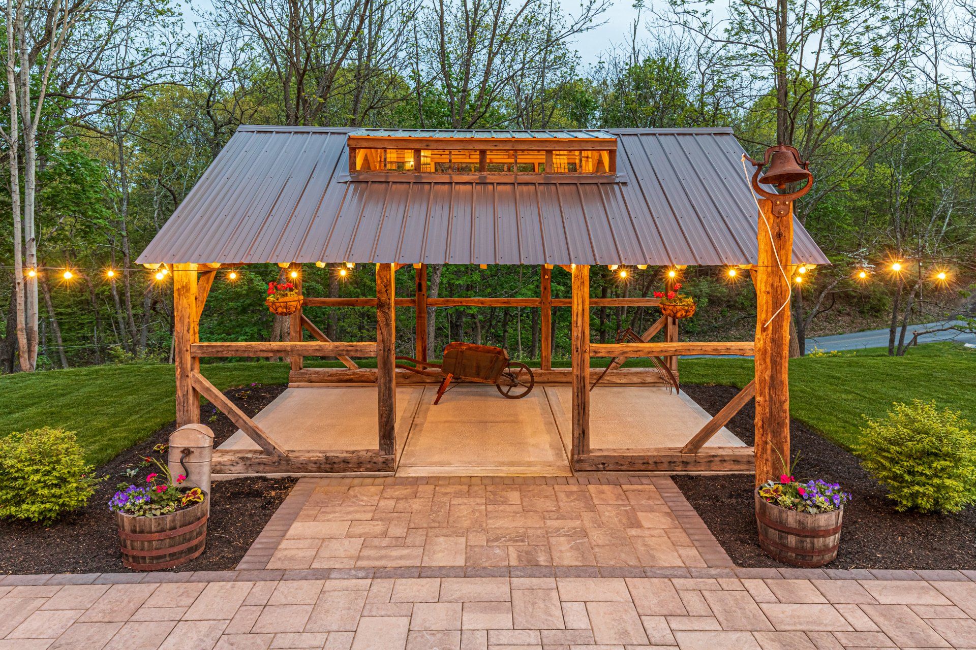 Rustic wooden gazebo with metal roof, fairy lights, and brick pathway.