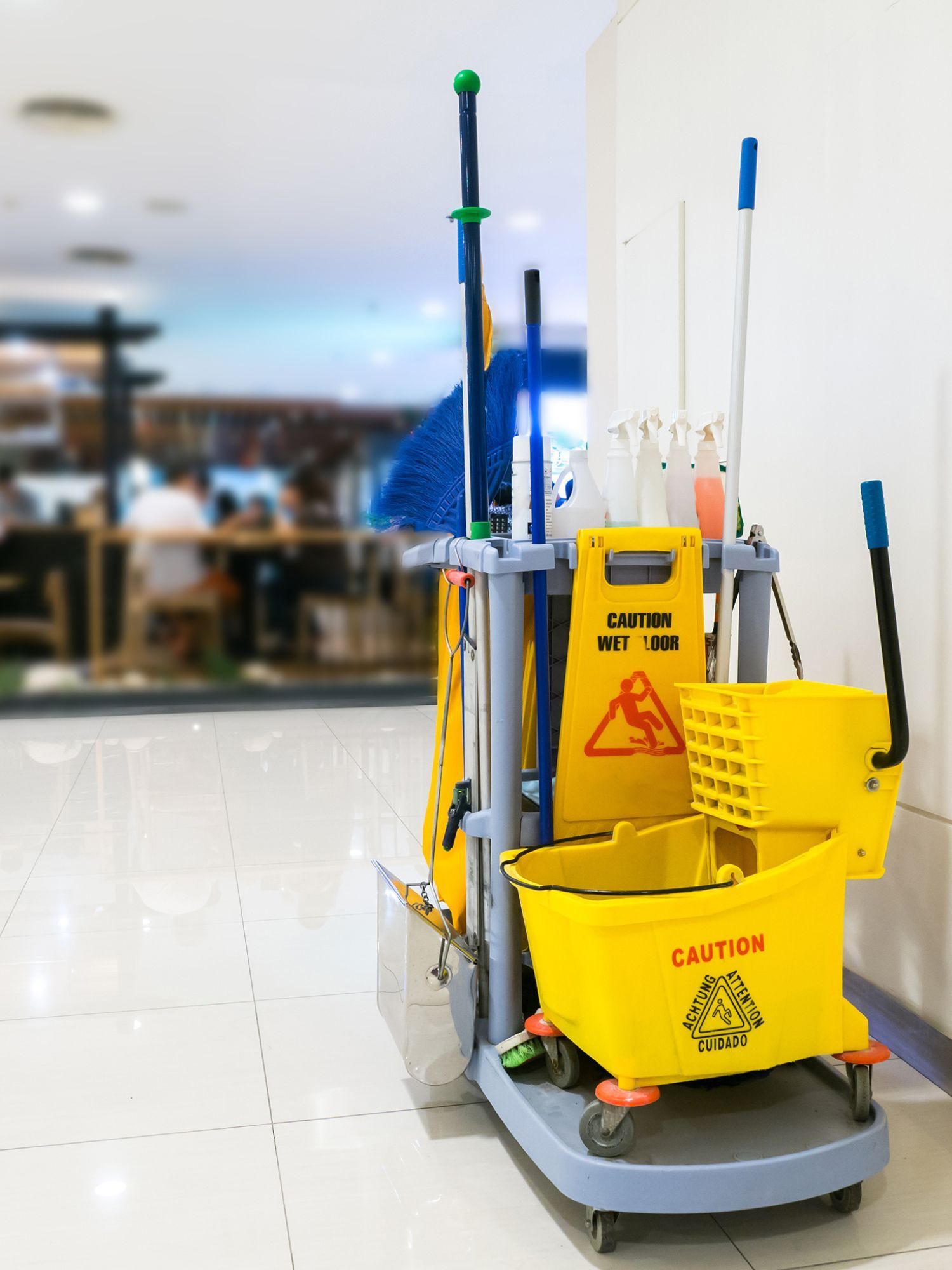 Yellow cleaning cart with caution sign, mops, and buckets in a hallway.