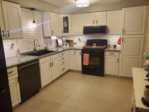 White kitchen with black appliances, grey countertops, and cream cabinets.