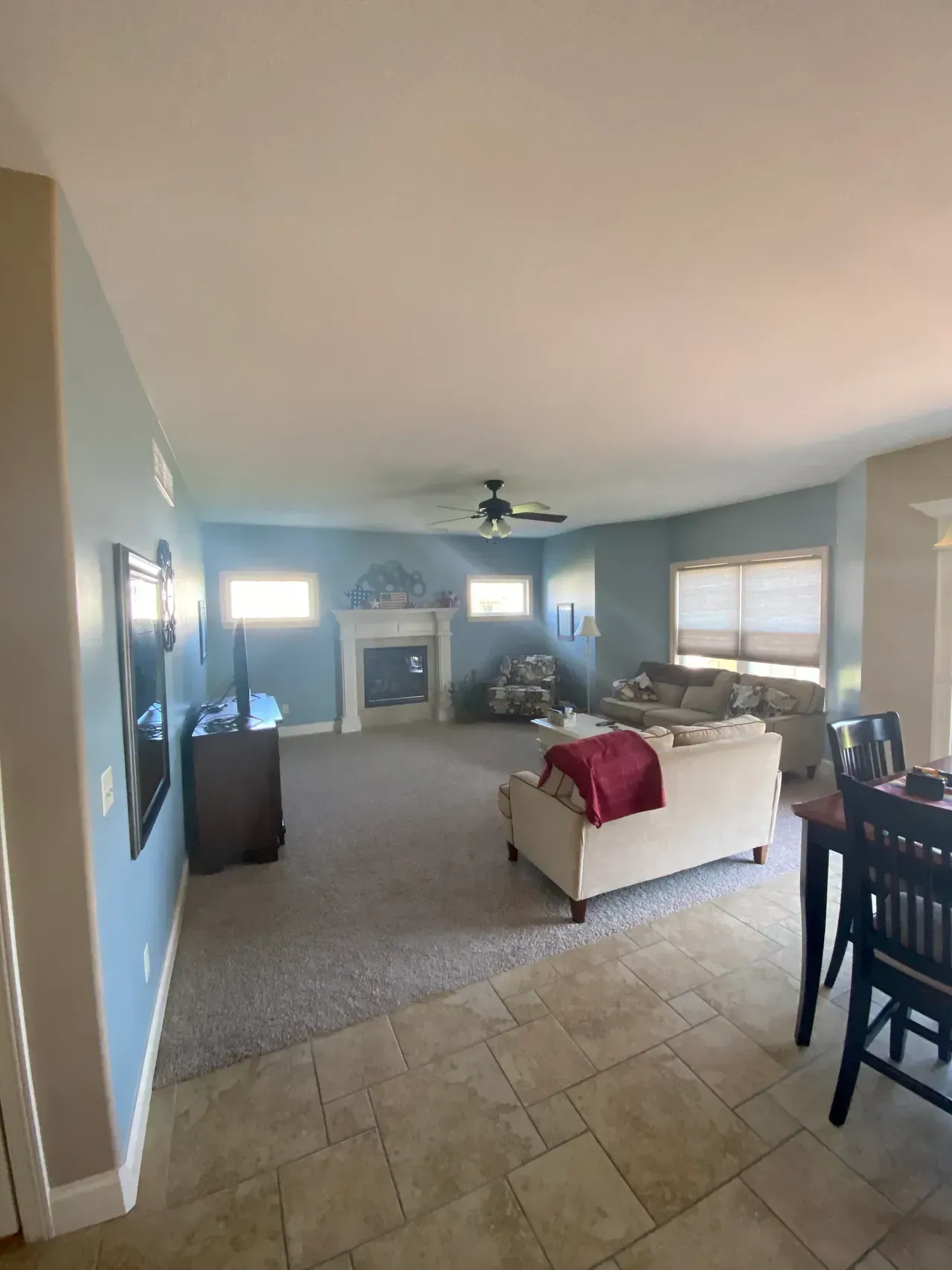Spacious living room with blue walls, fireplace, and sofa.  Beige carpet and tan tile flooring.