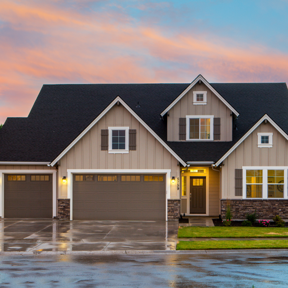Tan suburban house with dark roof, three-car garage, and stone accents, with colorful sunset sky.