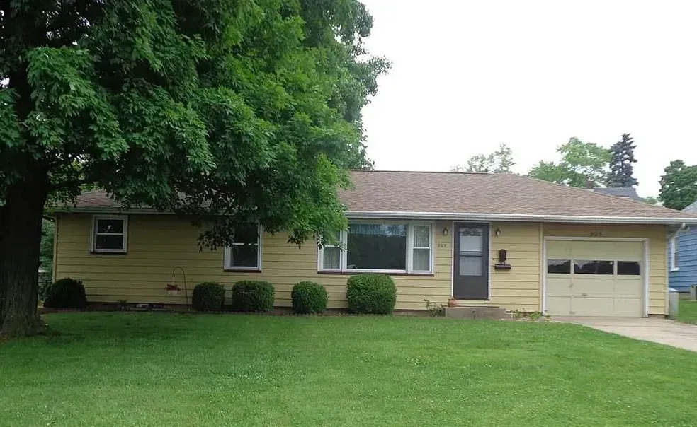 Yellow ranch-style house with a garage, green lawn, and a large tree in the front yard.