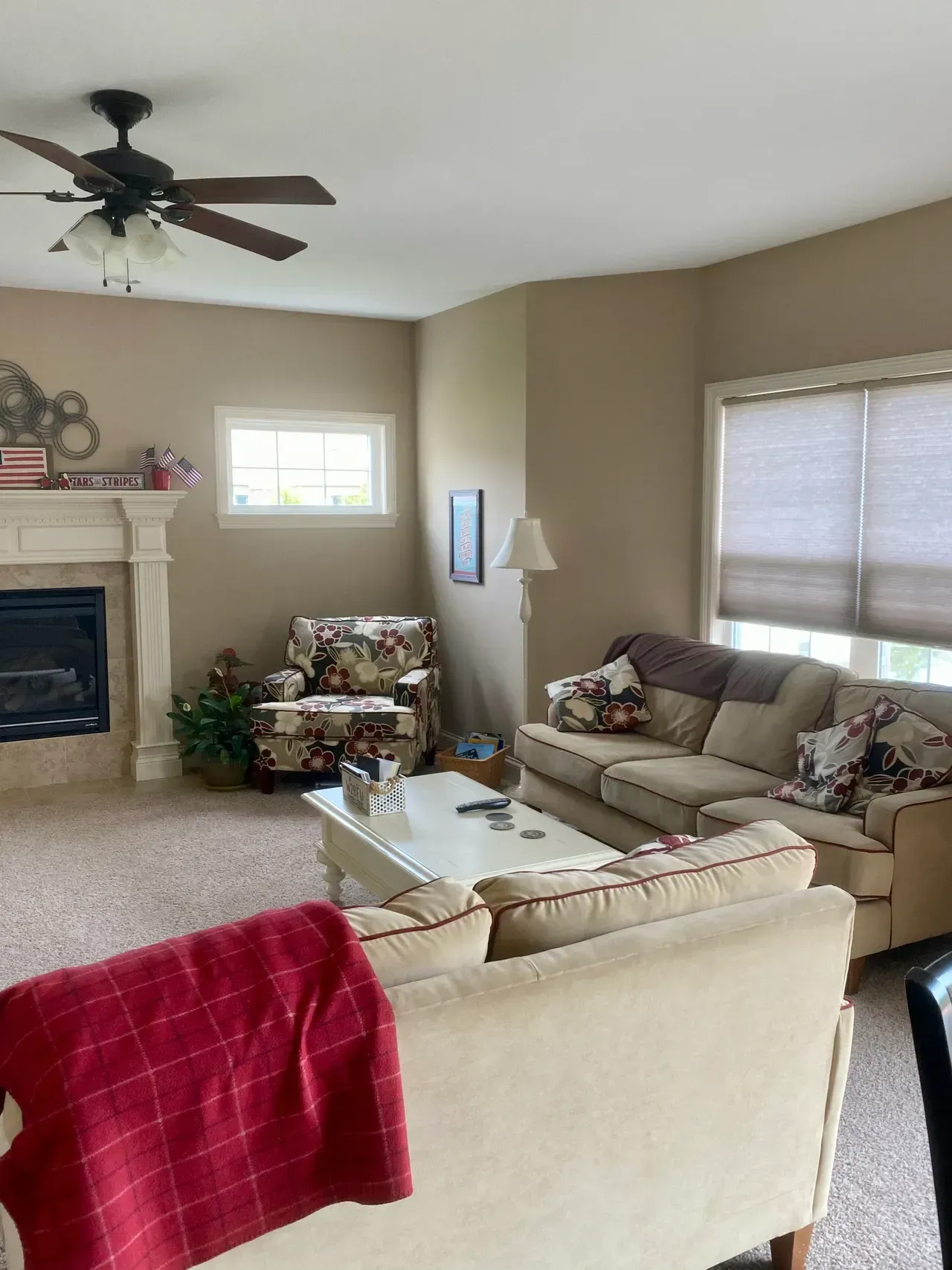 Cozy living room with beige walls, fireplace, floral patterned armchair and sofa, and a red blanket on a couch.