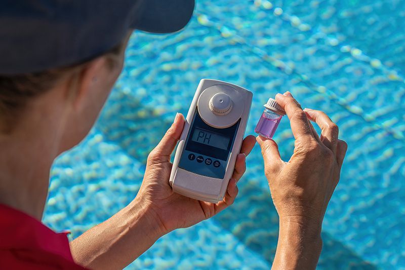 Pool technician checking water pH with a digital tester by the pool.