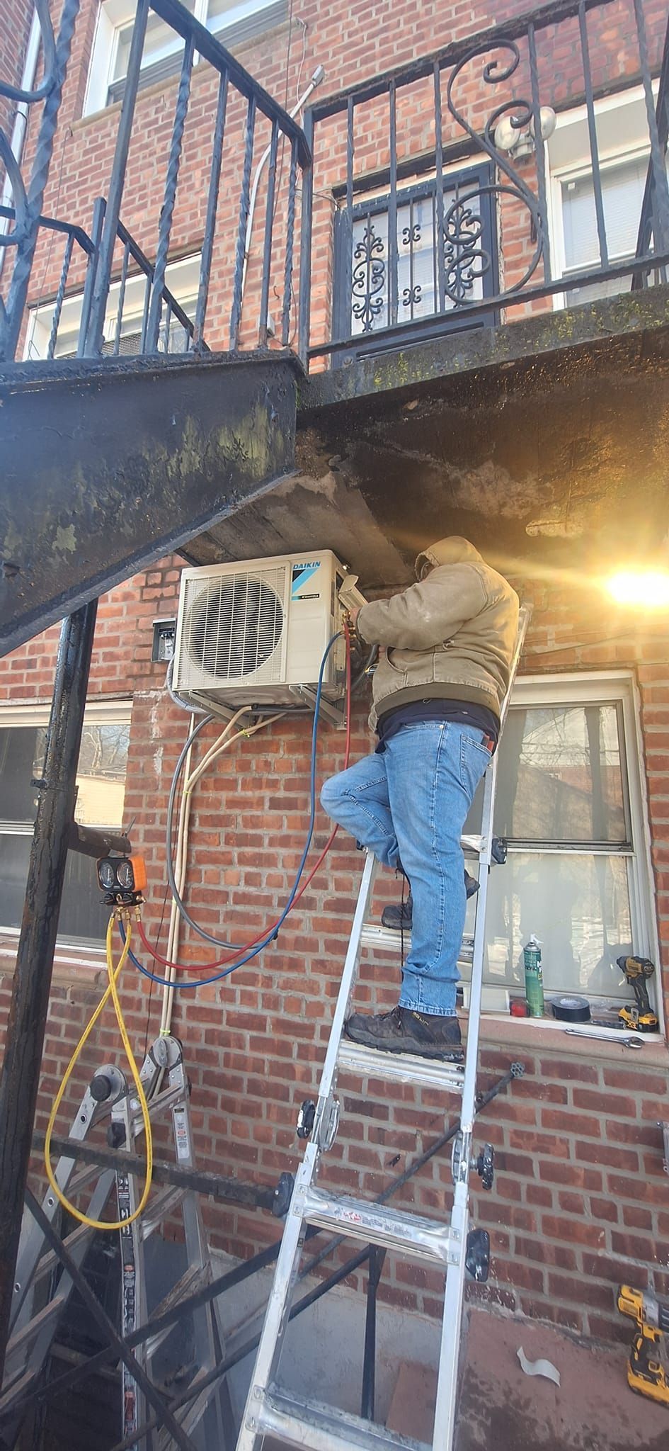 Person on ladder installing AC unit on brick building exterior.