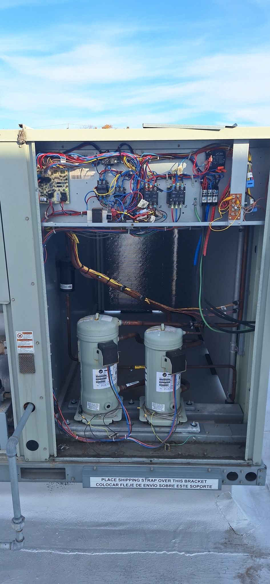 An open air conditioning unit with electrical components and two large compressors.