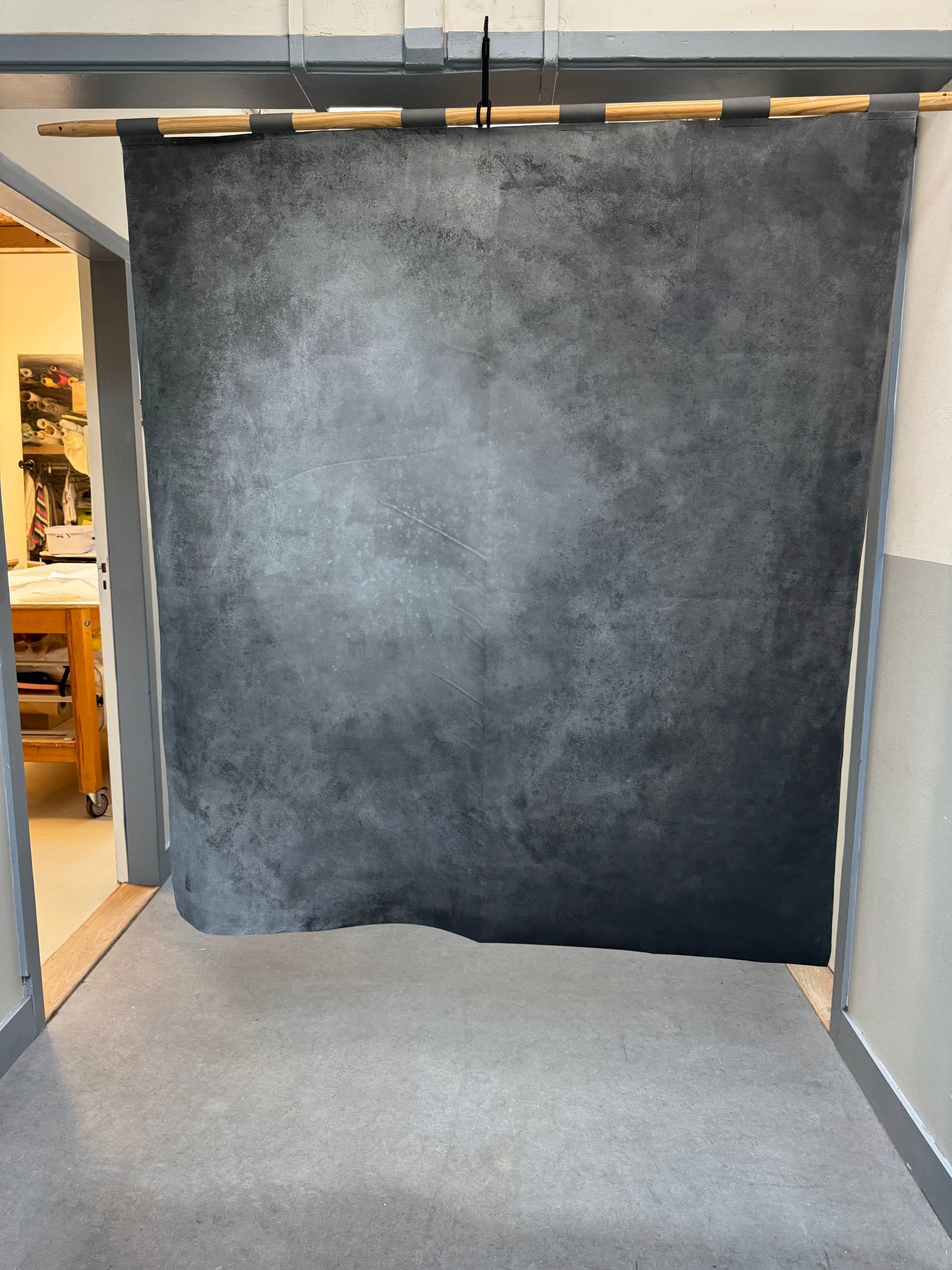 Groot, donkergrijs achtergronddoek met textuur hangt in een deuropening, mogelijk voor fotografie.