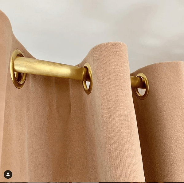 Perzikkleurig gordijn met gouden ringen, hangend aan een gouden stang, close-up.