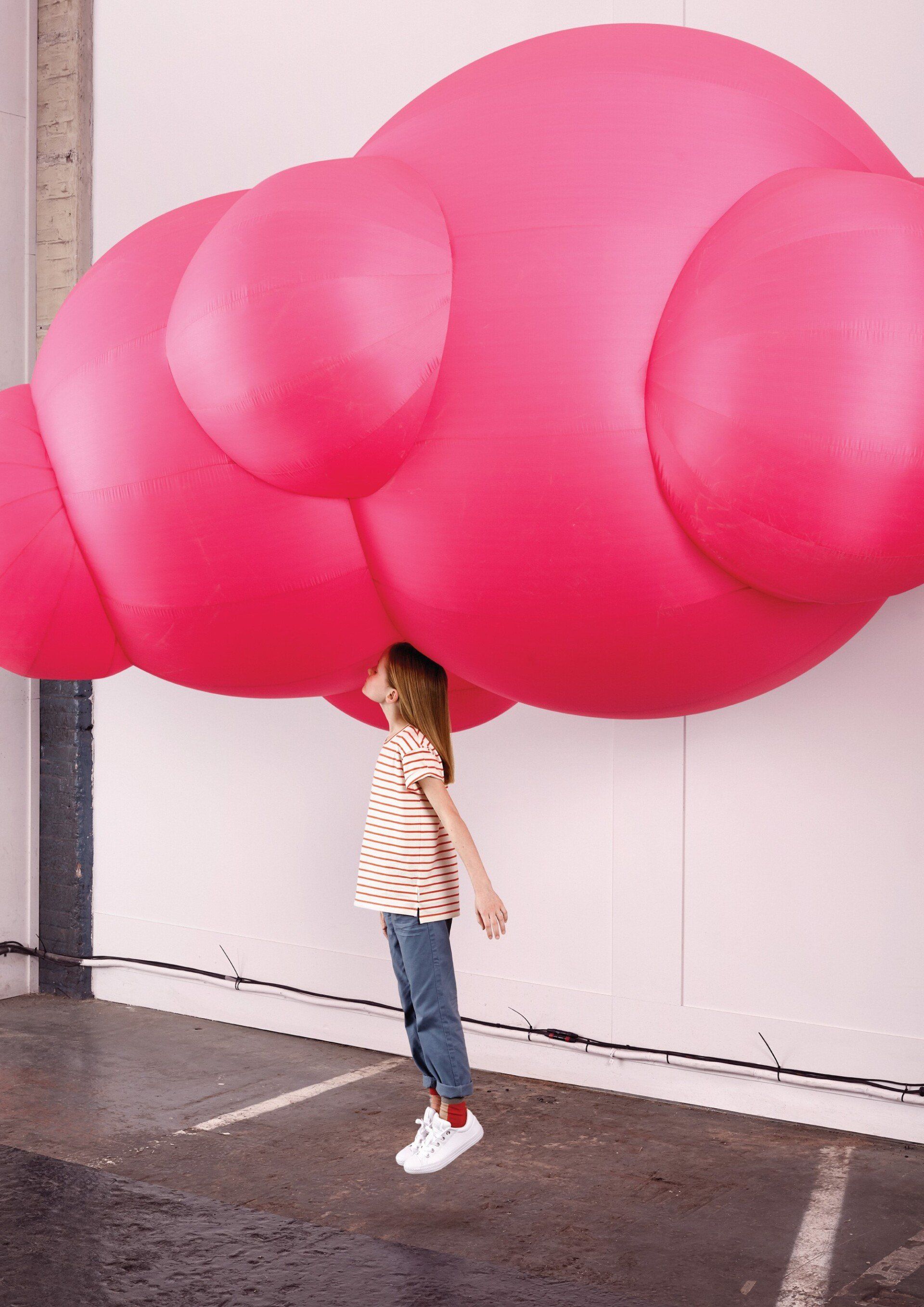 Meisje kijkt omhoog naar een groot, roze, opblaasbaar beeld in de vorm van een wolk.