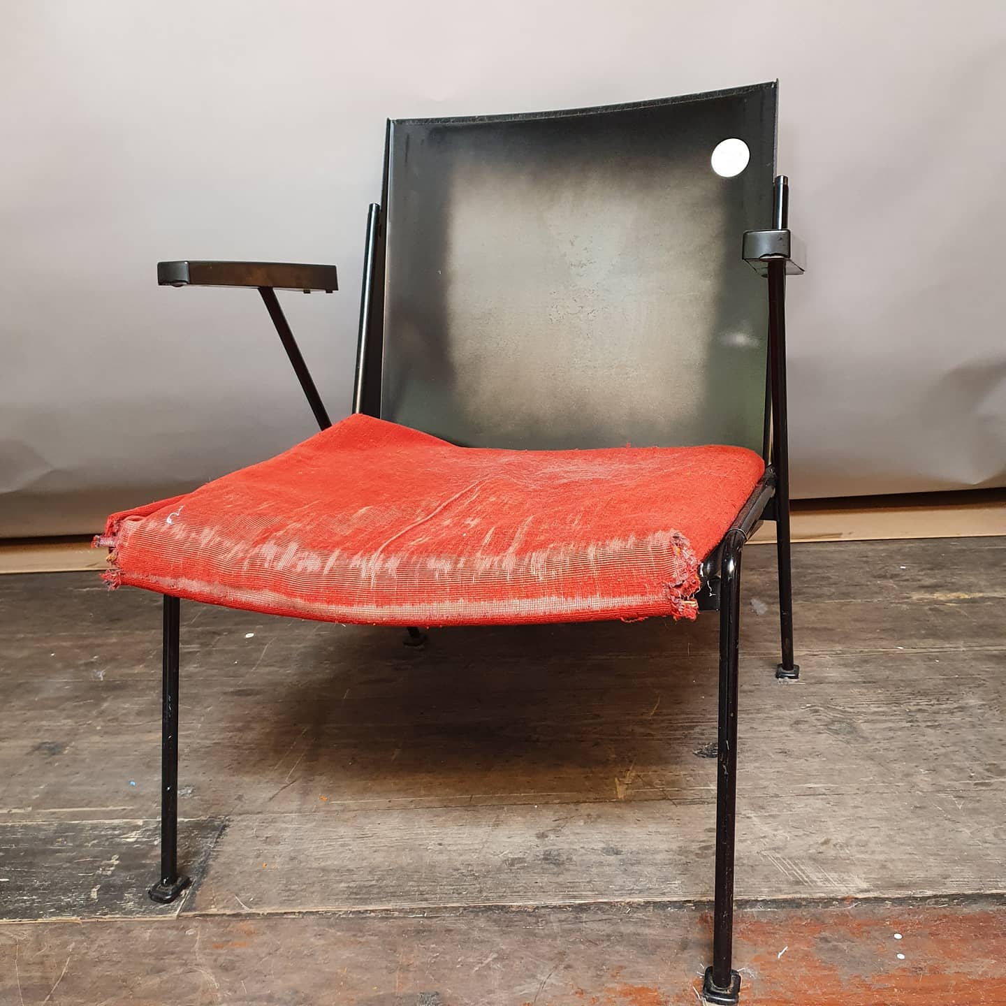 Zwarte metalen stoel met rood zitkussen en armleuning.