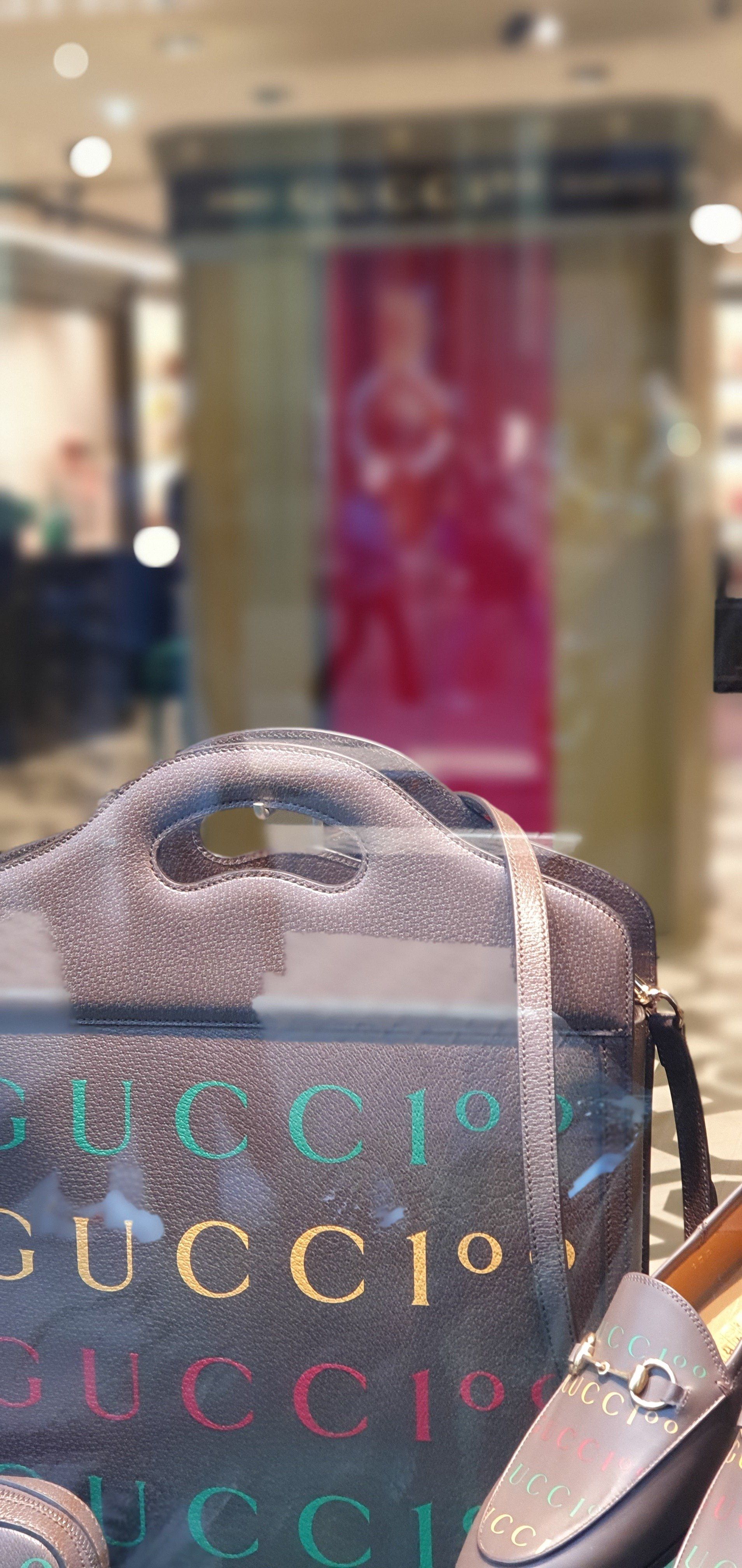 Glinsterende Gucci-tas in een etalage, met kleurrijk logo en loafers.