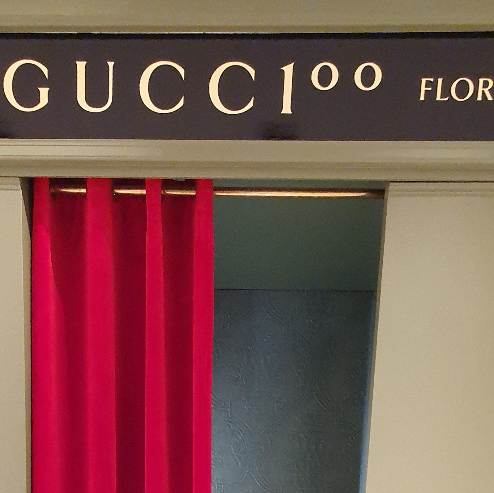 Gucci-winkelbord boven rode gordijndeur, Gucci 100-logo.
