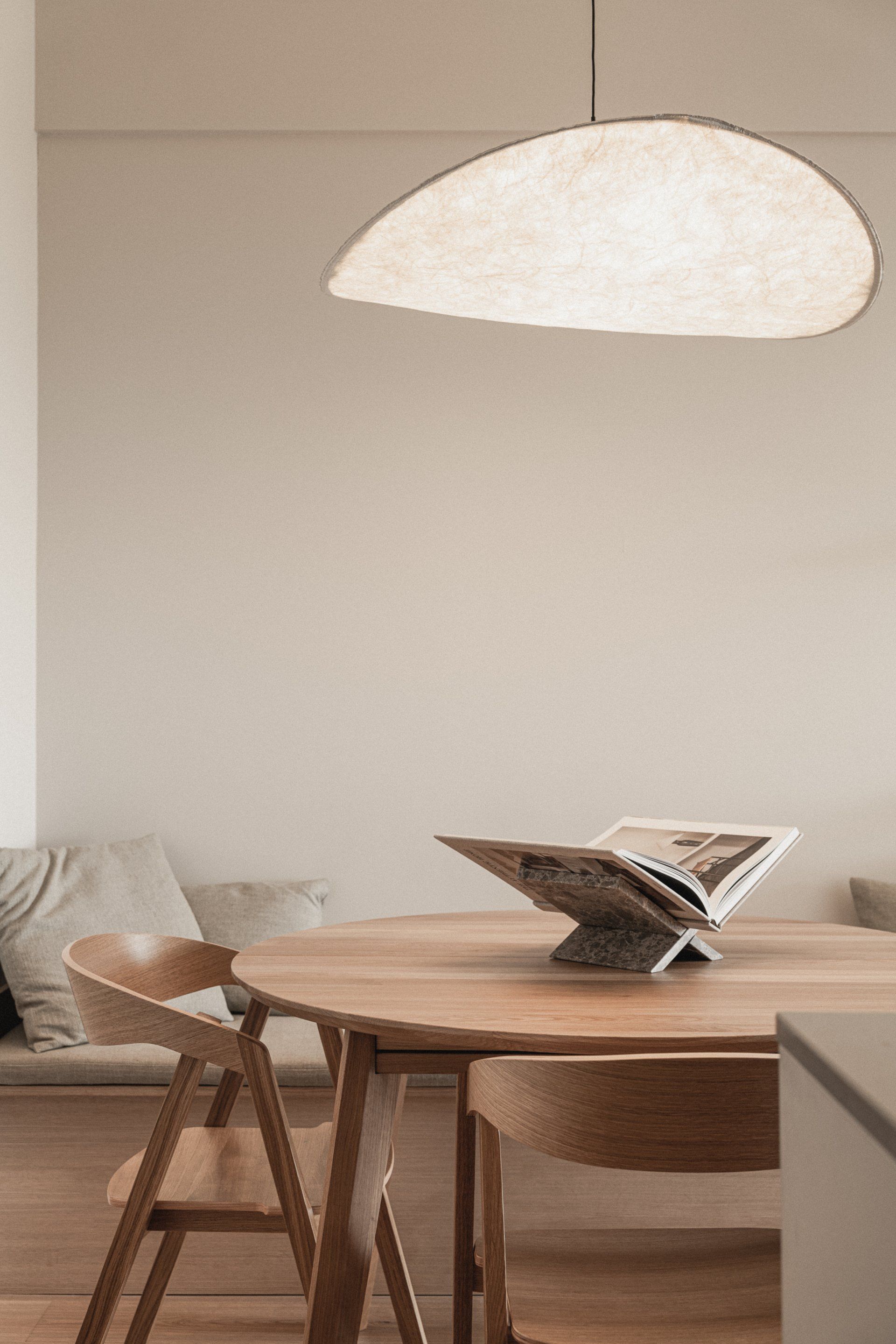 Ronde houten eettafel met twee stoelen en daarboven een papieren hanglamp.