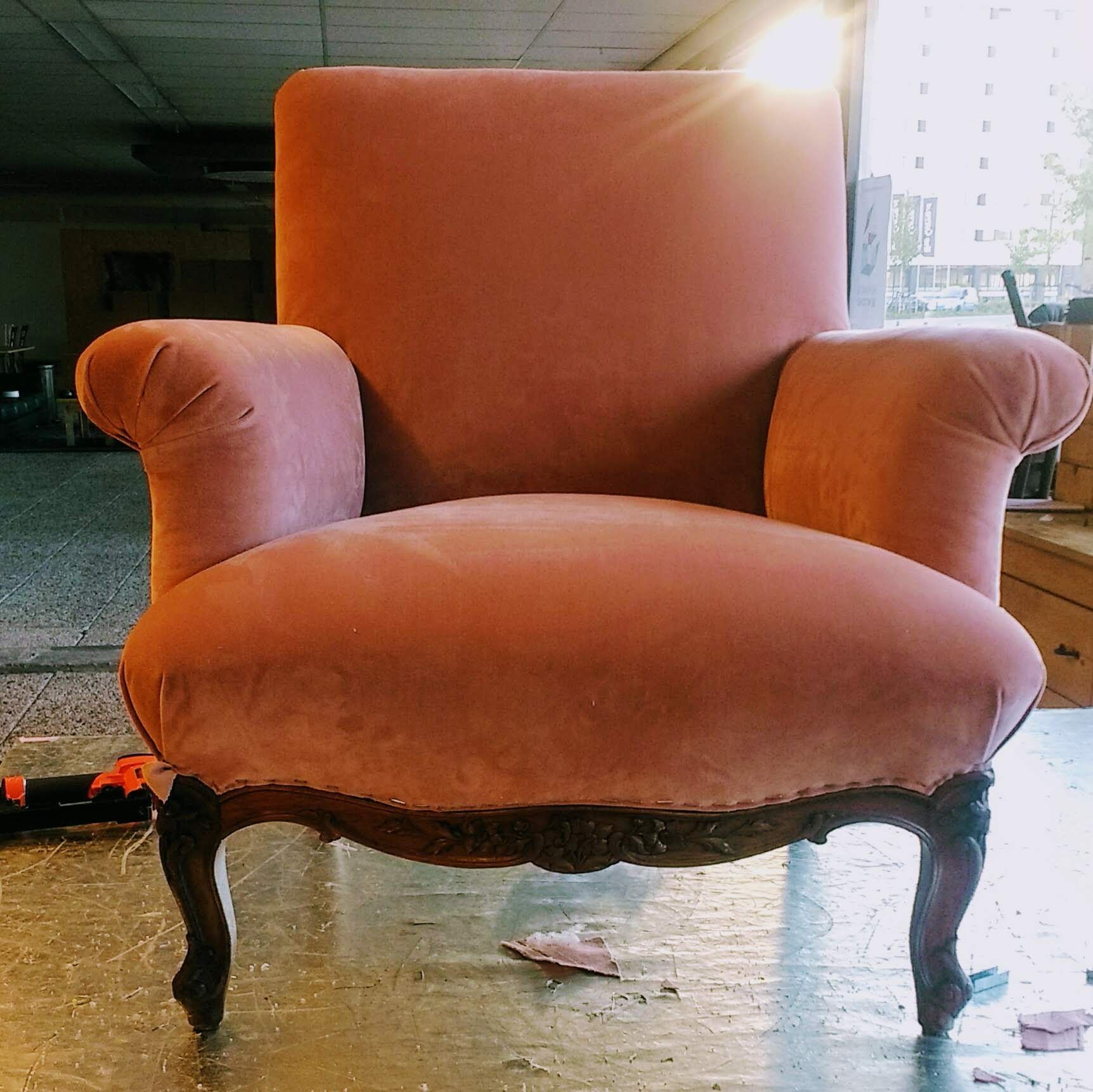 Roze fluwelen fauteuil met donker gesneden houten frame.