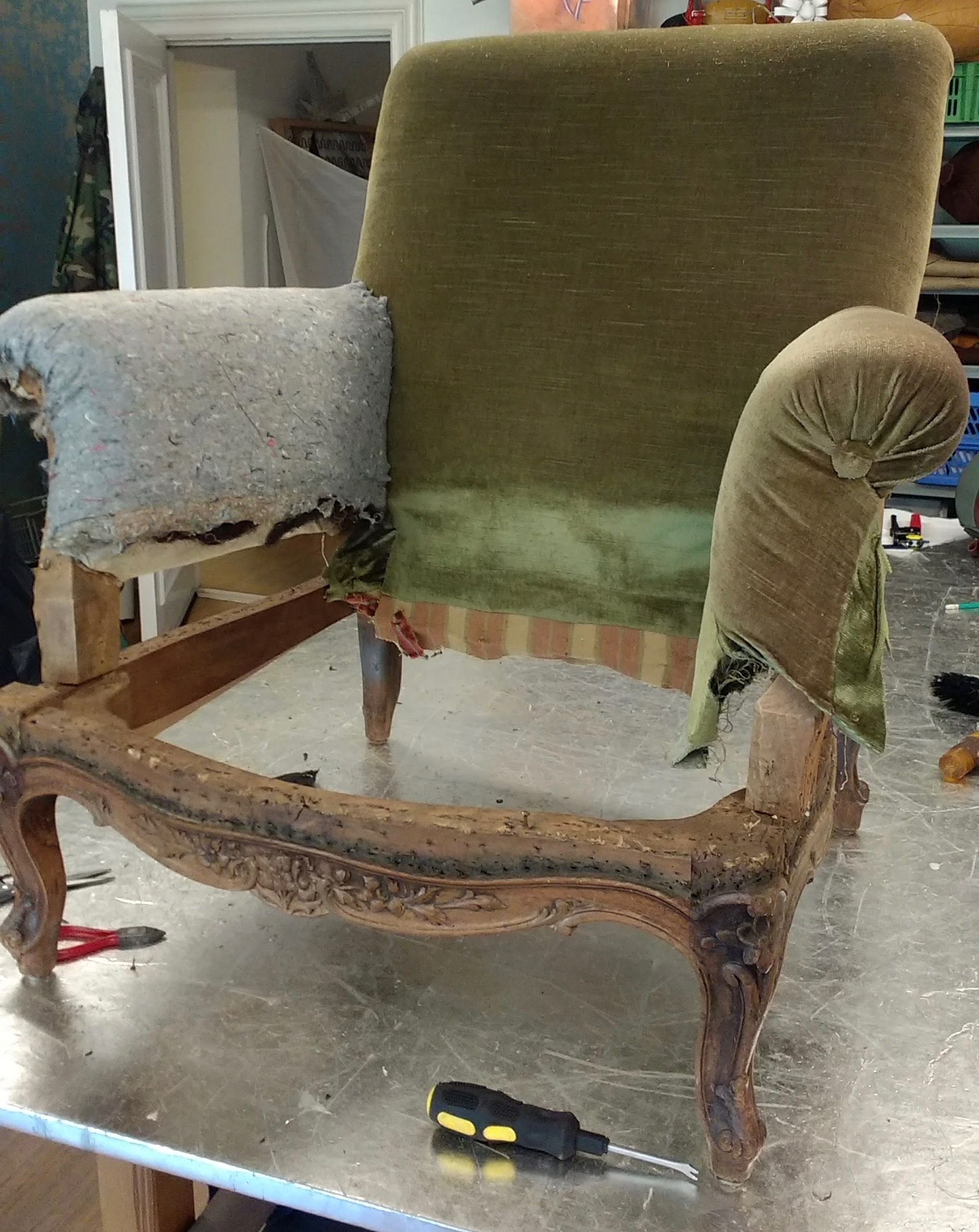 Een antiek stoelframe, gedeeltelijk bekleed, staat op een werktafel.