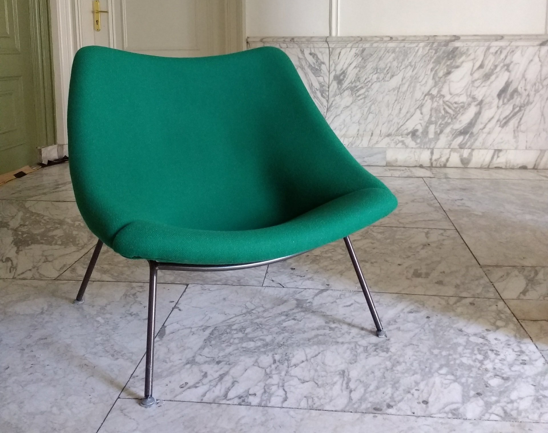 Groen beklede oyster stoel met slanke metalen poten op een marmeren vloer.