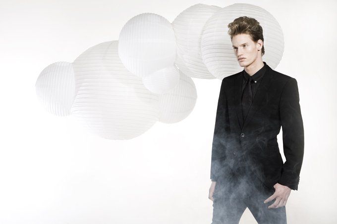 Een man in een zwart jasje, met witte papieren wolk op de achtergrond, wat rokerige mist aan zijn voeten.