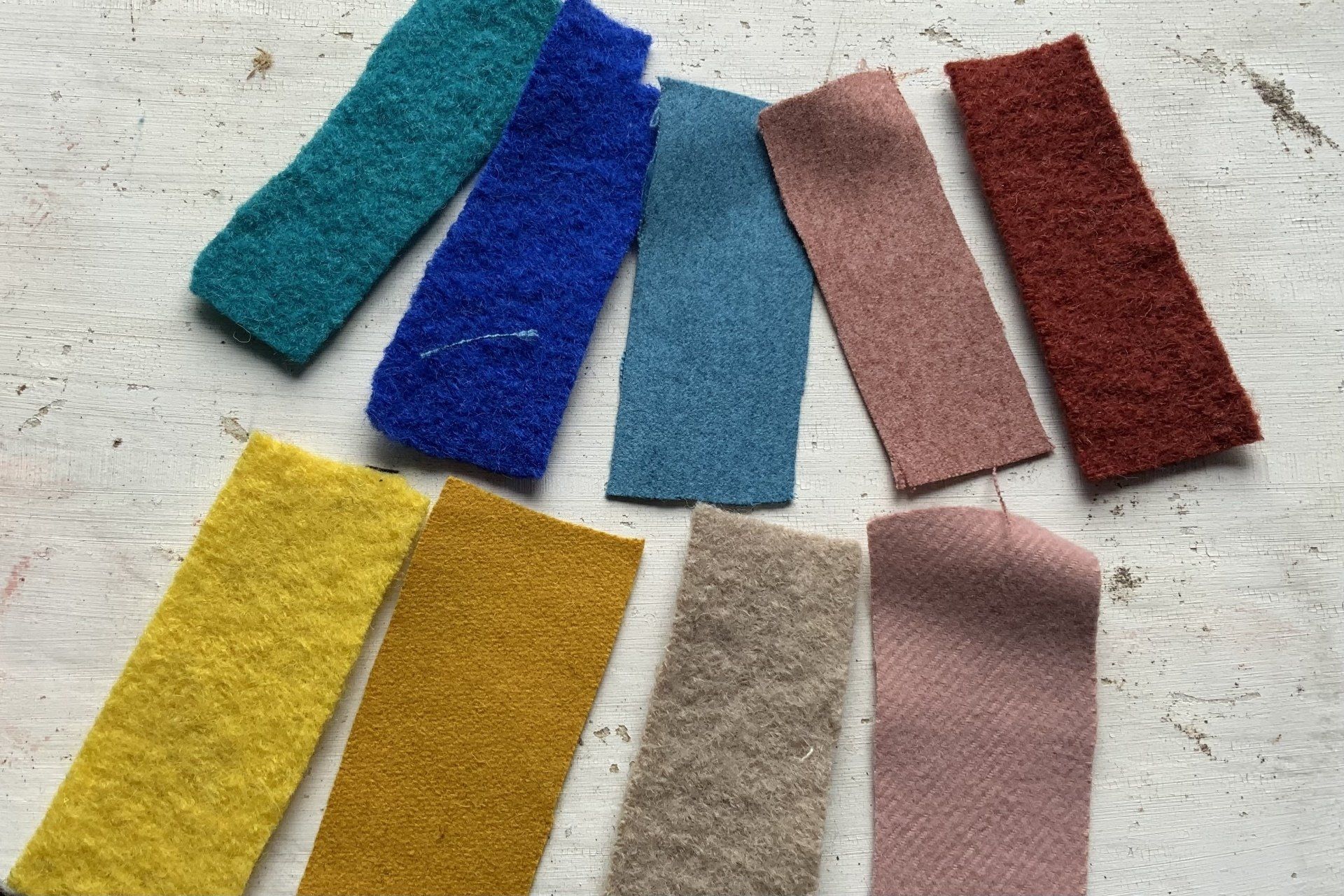Negen rechthoekige, kleurrijke,  stofstalen: blauwgroen, blauw, beige, roze, rood, geel, goud, grijs en roze.
