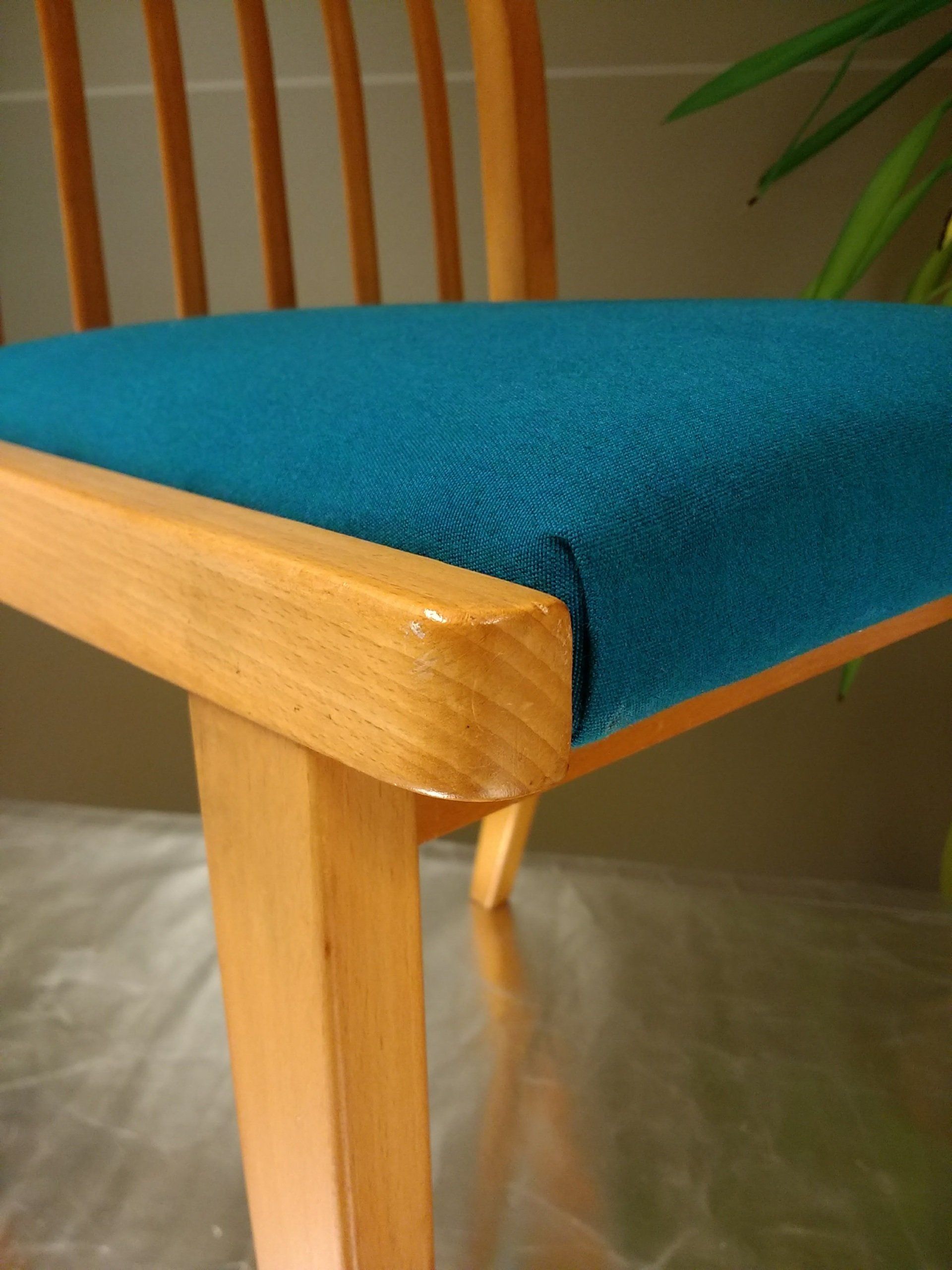 Houten stoel met een blauwgroene gestoffeerde zitting, een licht houten frame en een gespleten rugleuning.