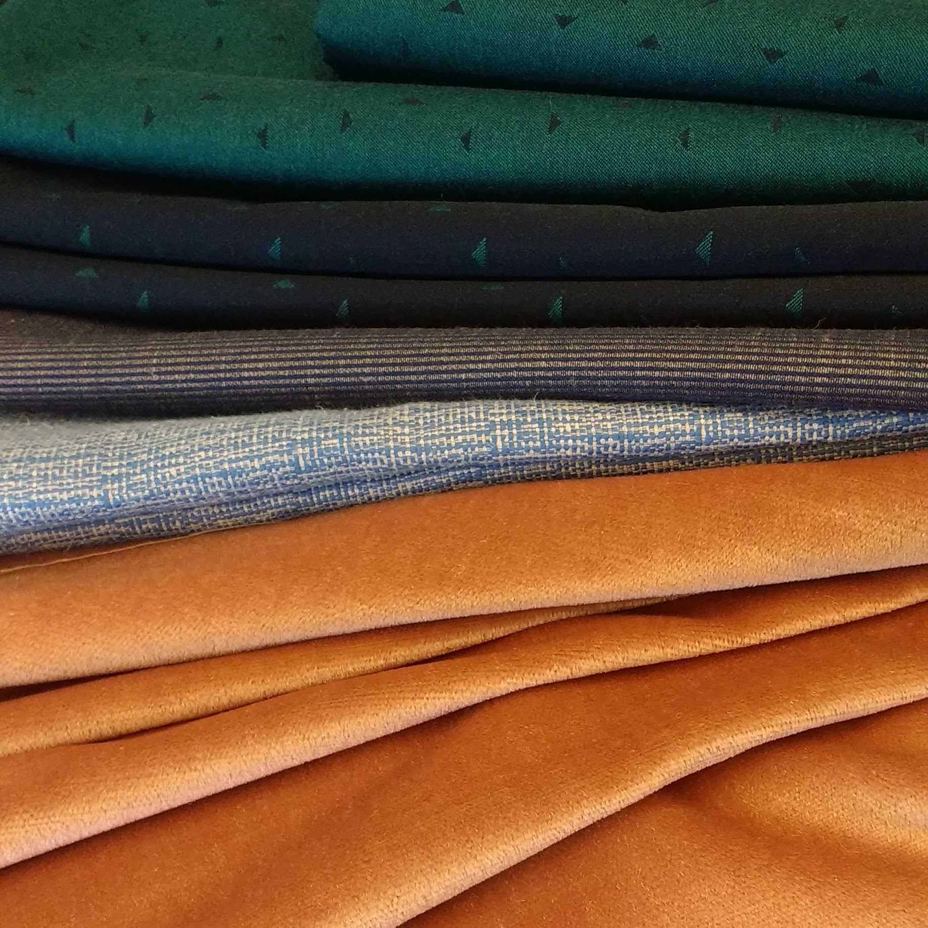 Stapel verschillende stoffen in tinten groen, blauw, zilver en oranje.