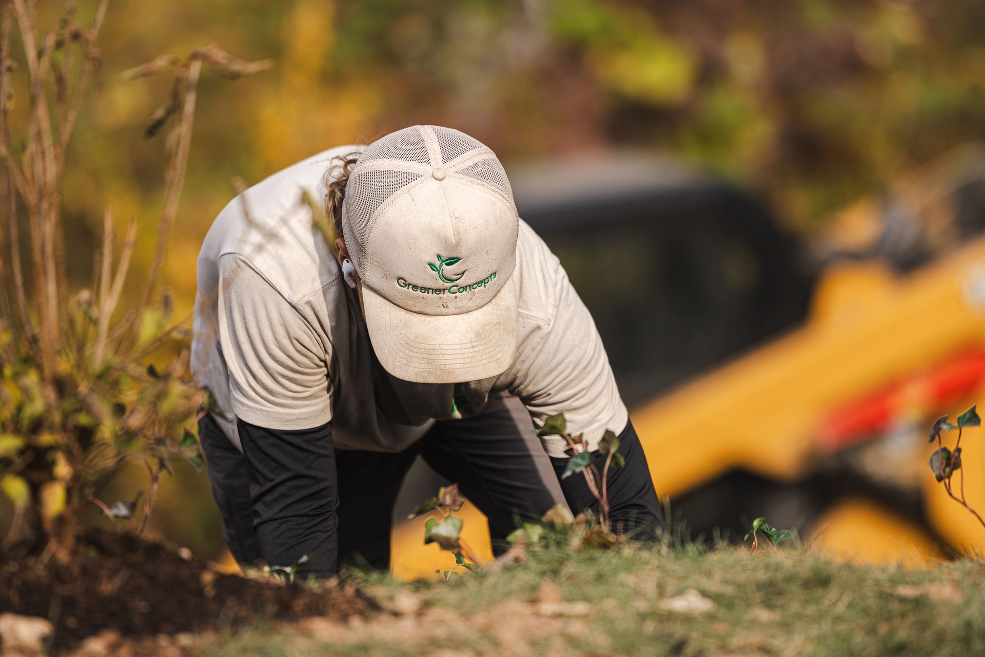 A man wearing a hat is kneeling down in the dirt.