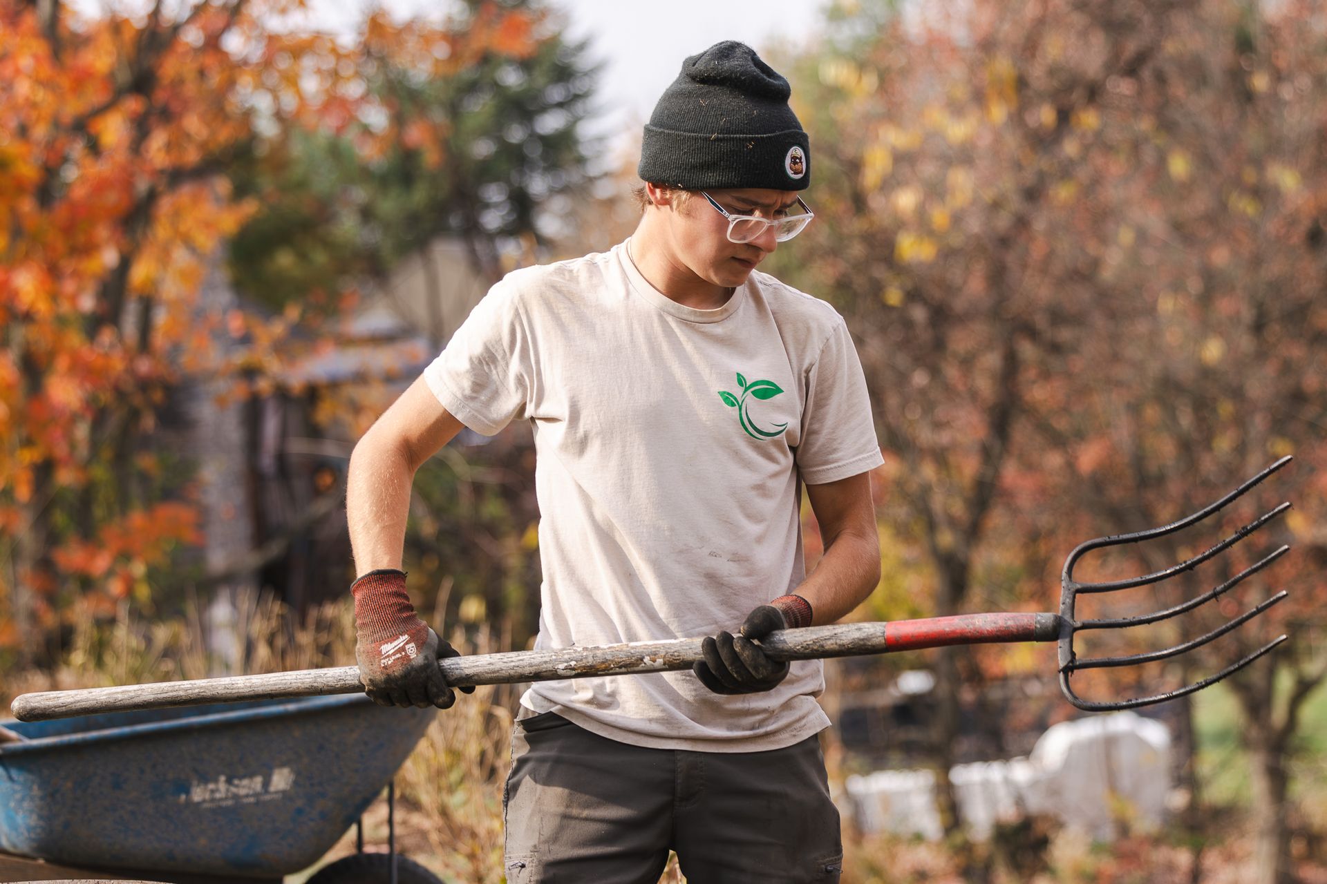 A man is holding a rake next to a wheelbarrow.