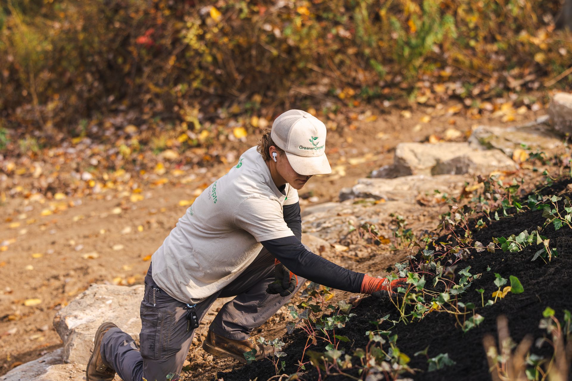 A man is kneeling down in the dirt while working in a garden.