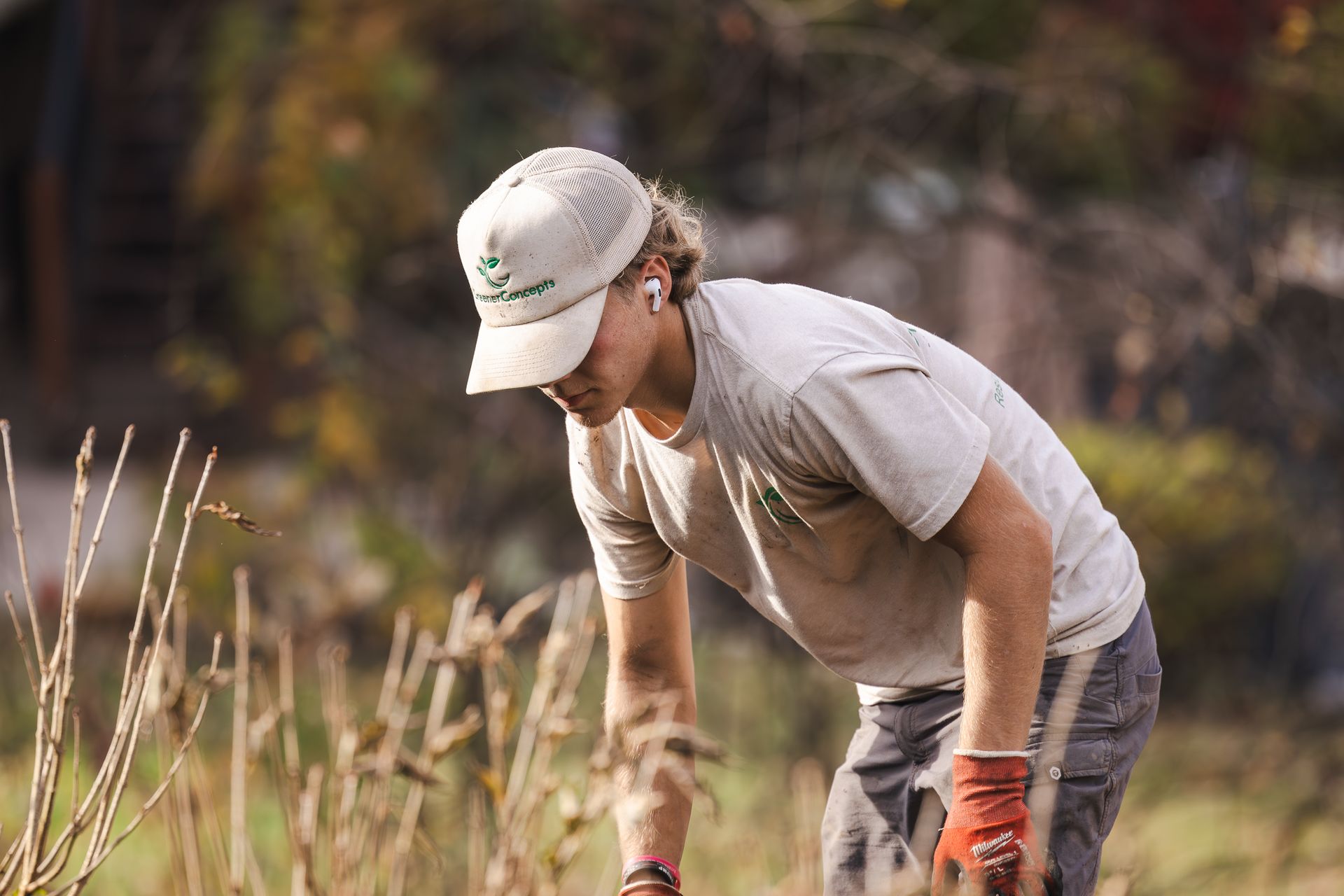 A man wearing a hat and gloves is kneeling down in a field.