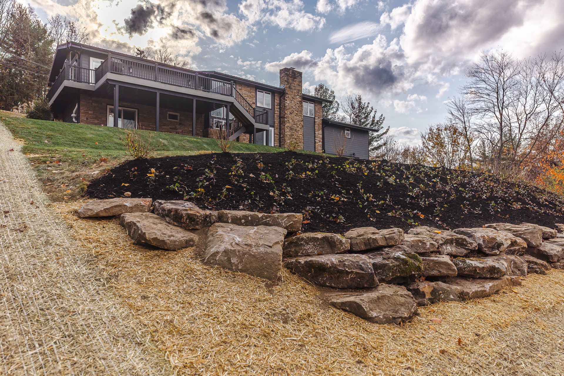 A large house is sitting on top of a hill surrounded by trees and rocks.