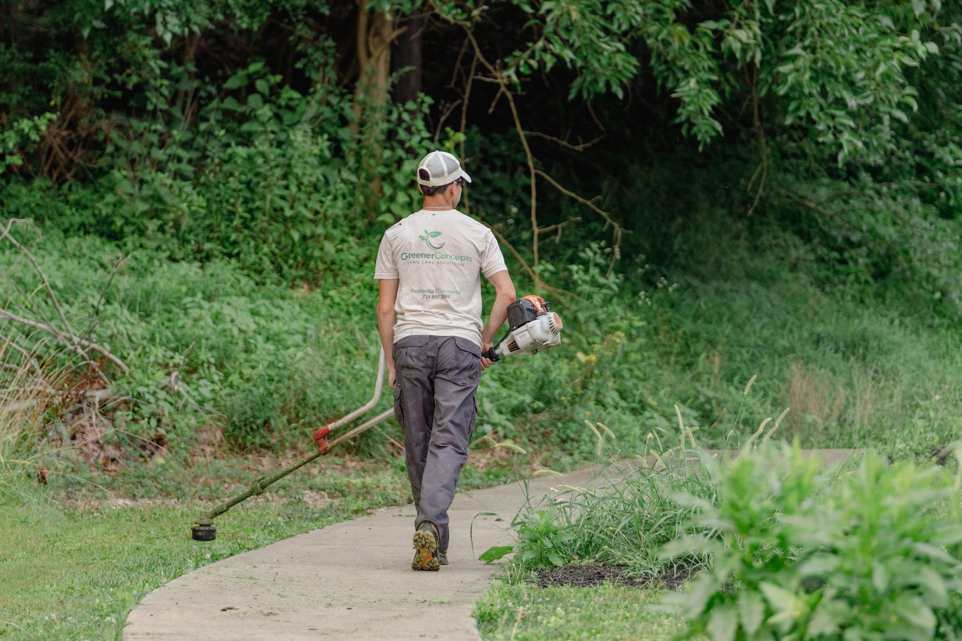 A man is walking down a path while holding a lawn mower.