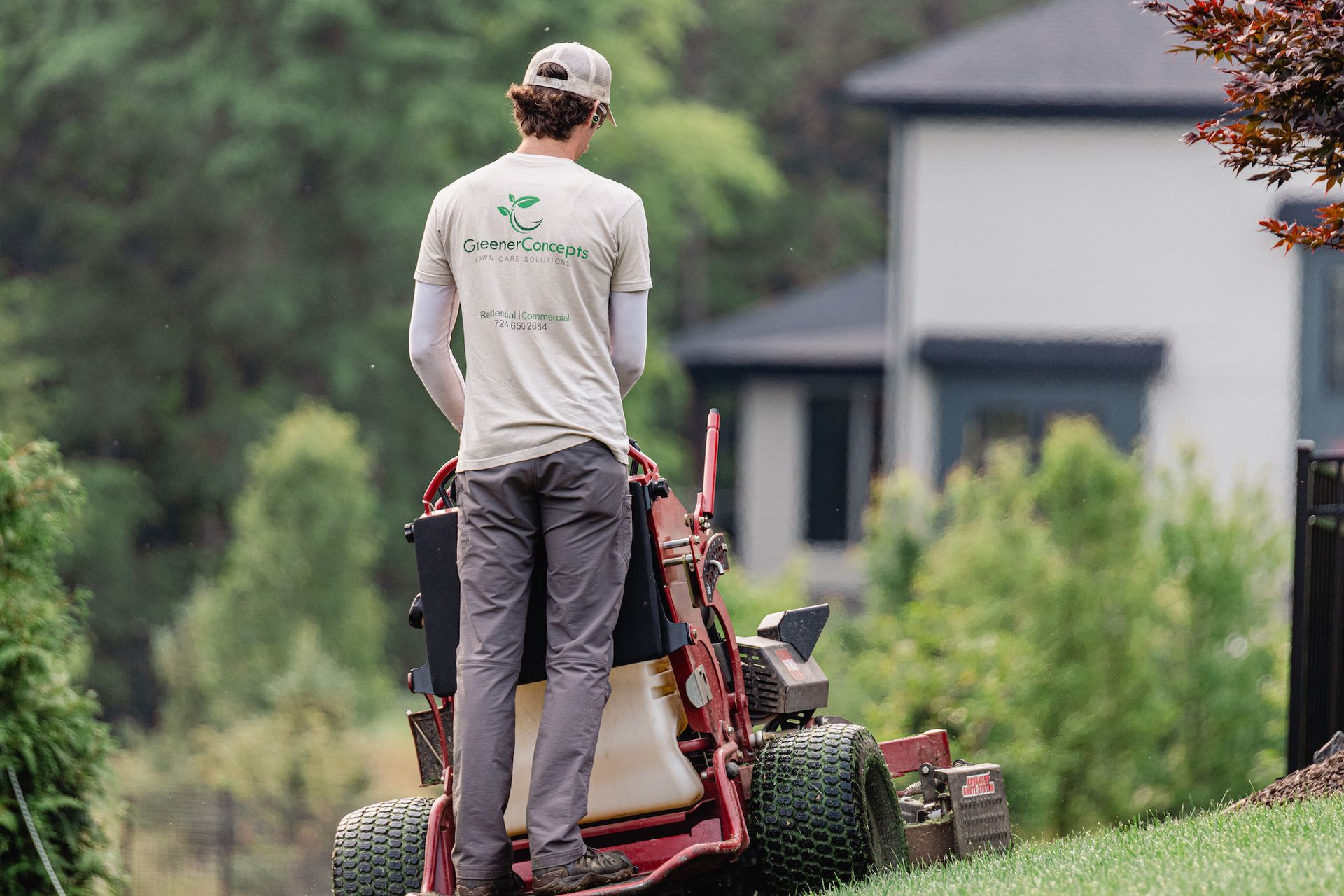 A man is standing next to a lawn mower in front of a house.