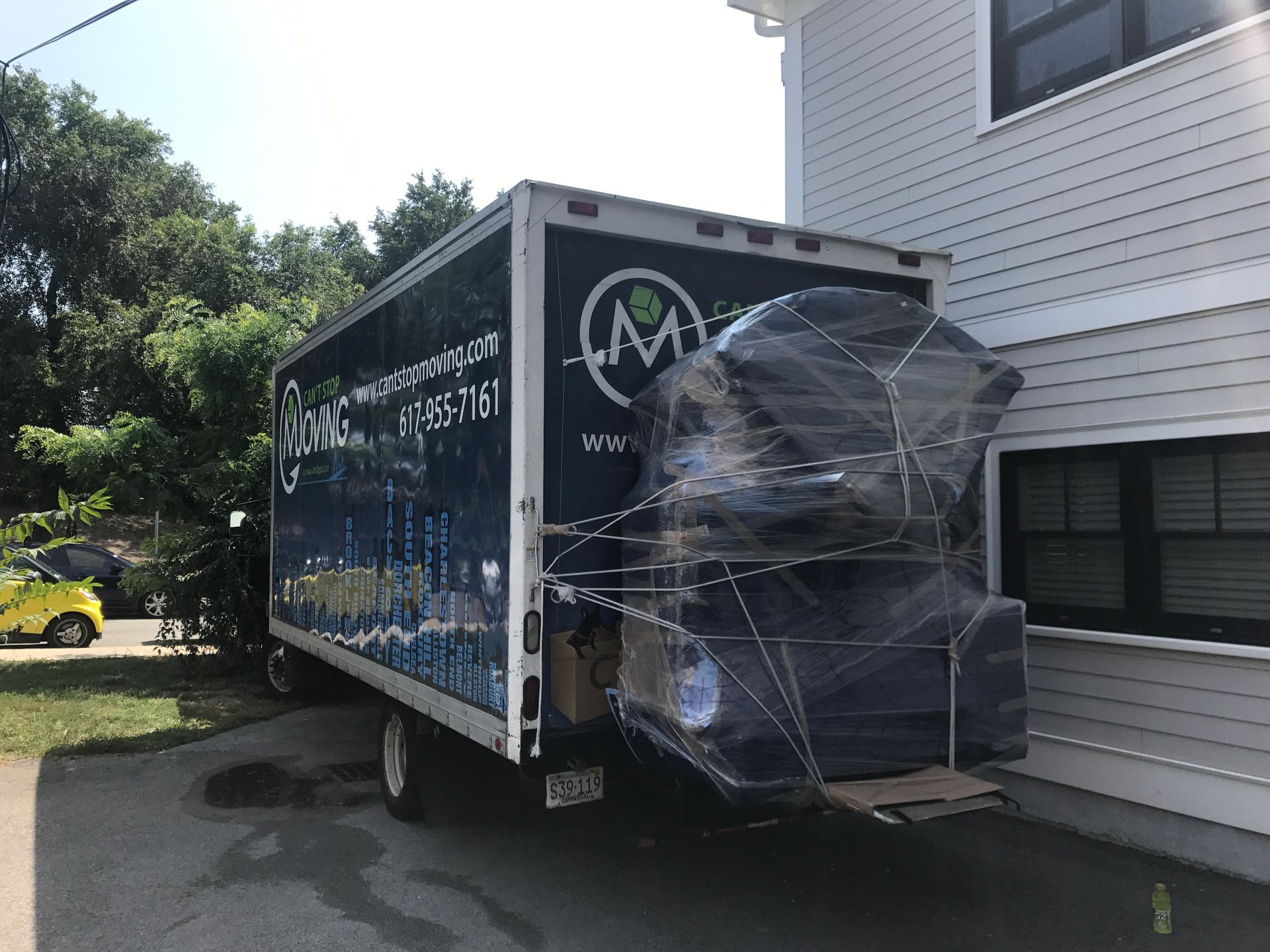 Moving truck parked next to a house with furniture wrapped in plastic.
