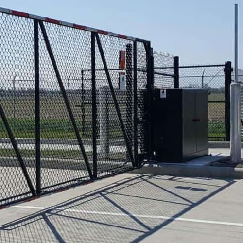 A sliding gate is sitting on the side of a road next to a fence.