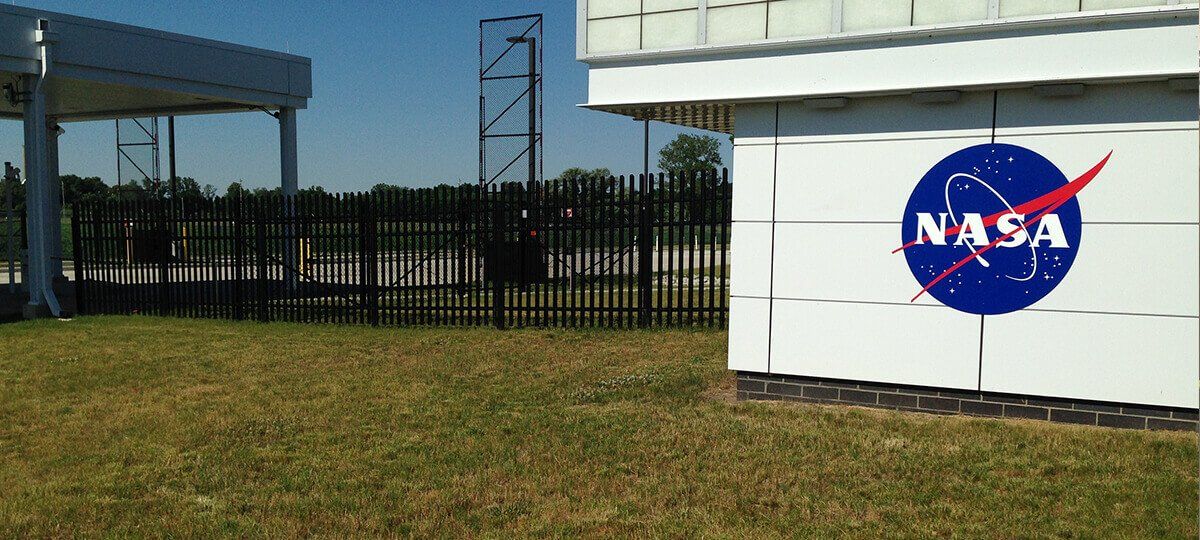A nasa sign is sitting in the grass next to a fence.