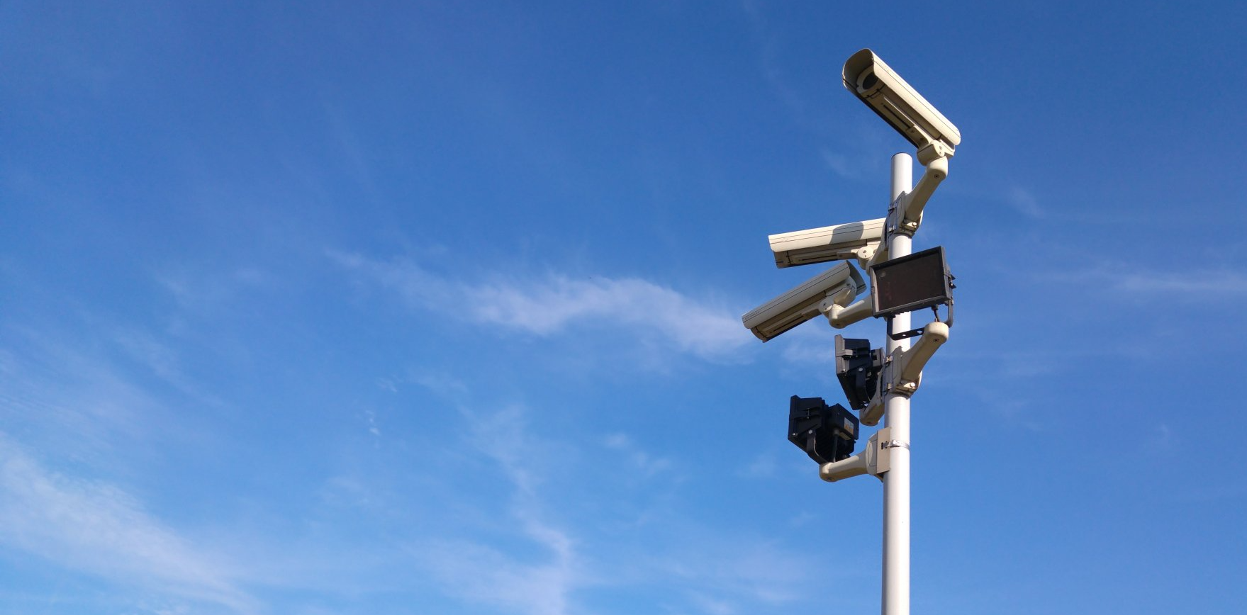 A bunch of security cameras on a pole against a blue sky.