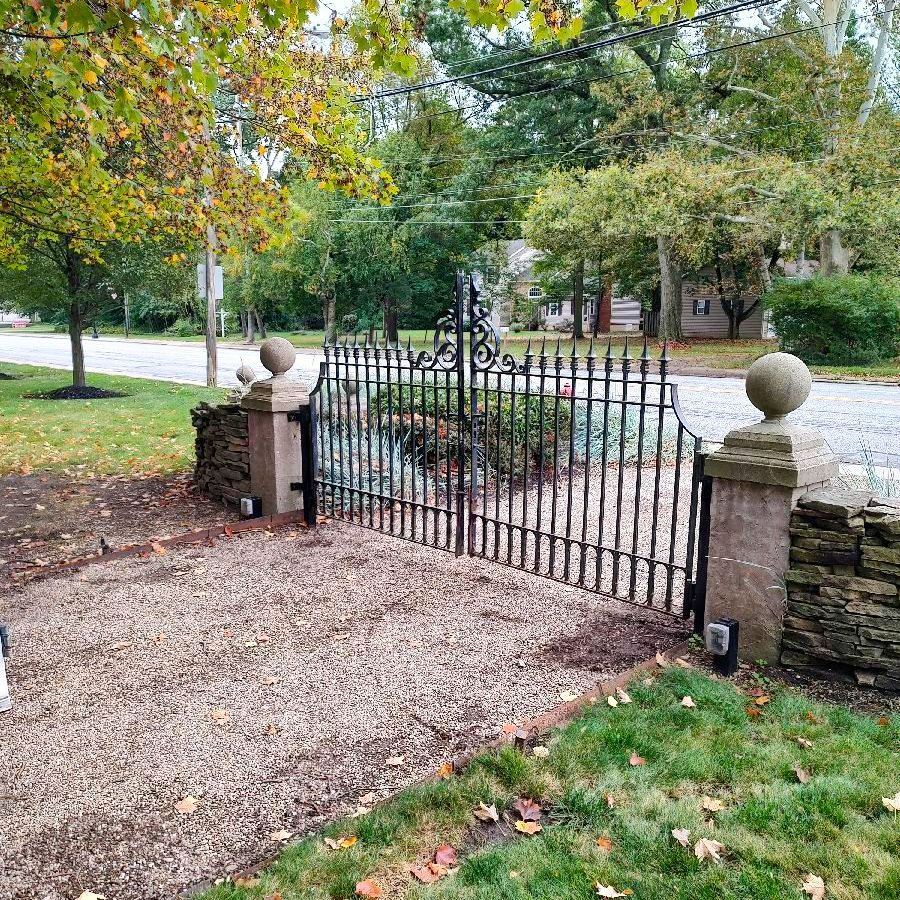 A wrought iron gate is sitting in the middle of a gravel driveway.