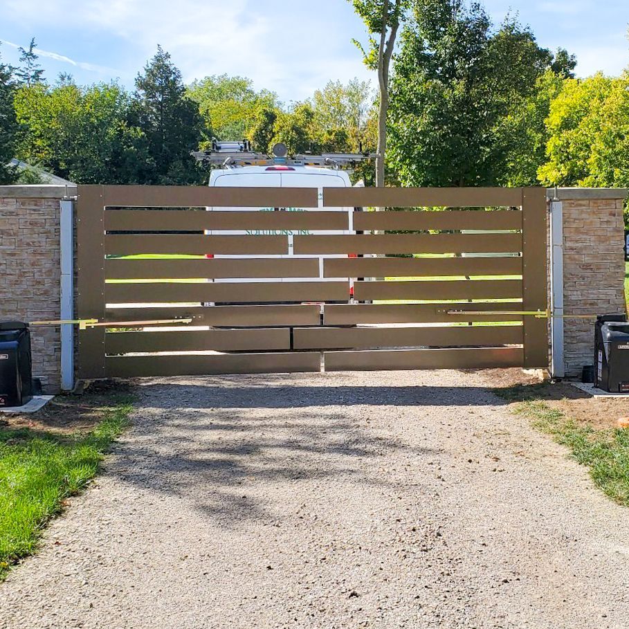 A large wooden gate is open to a gravel driveway.