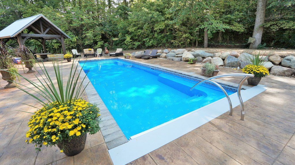 Rectangular blue pool surrounded by a patio, gazebo, and landscaping.