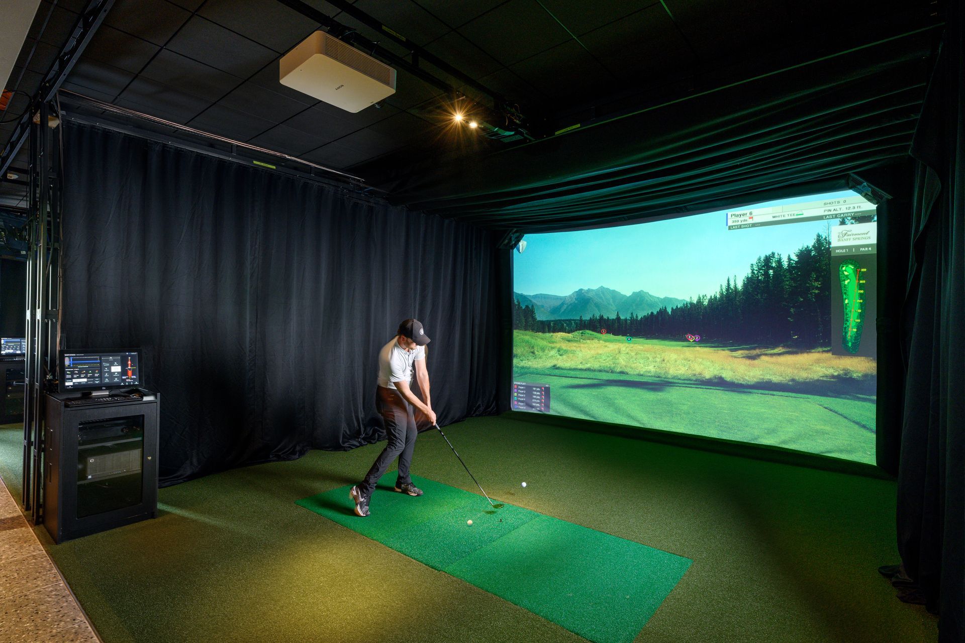 A man is swinging a golf club in a golf simulator.