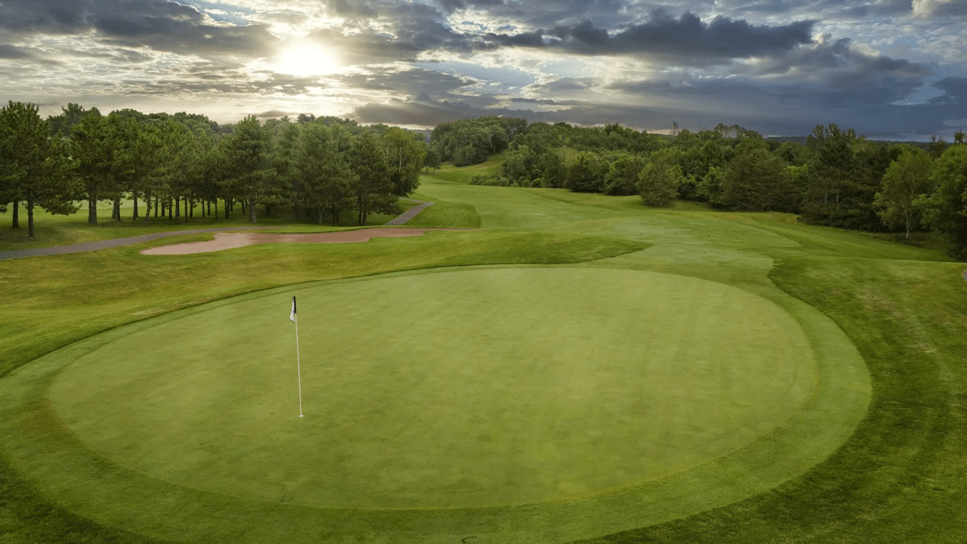 An aerial view of a golf course with a green and trees in the background.