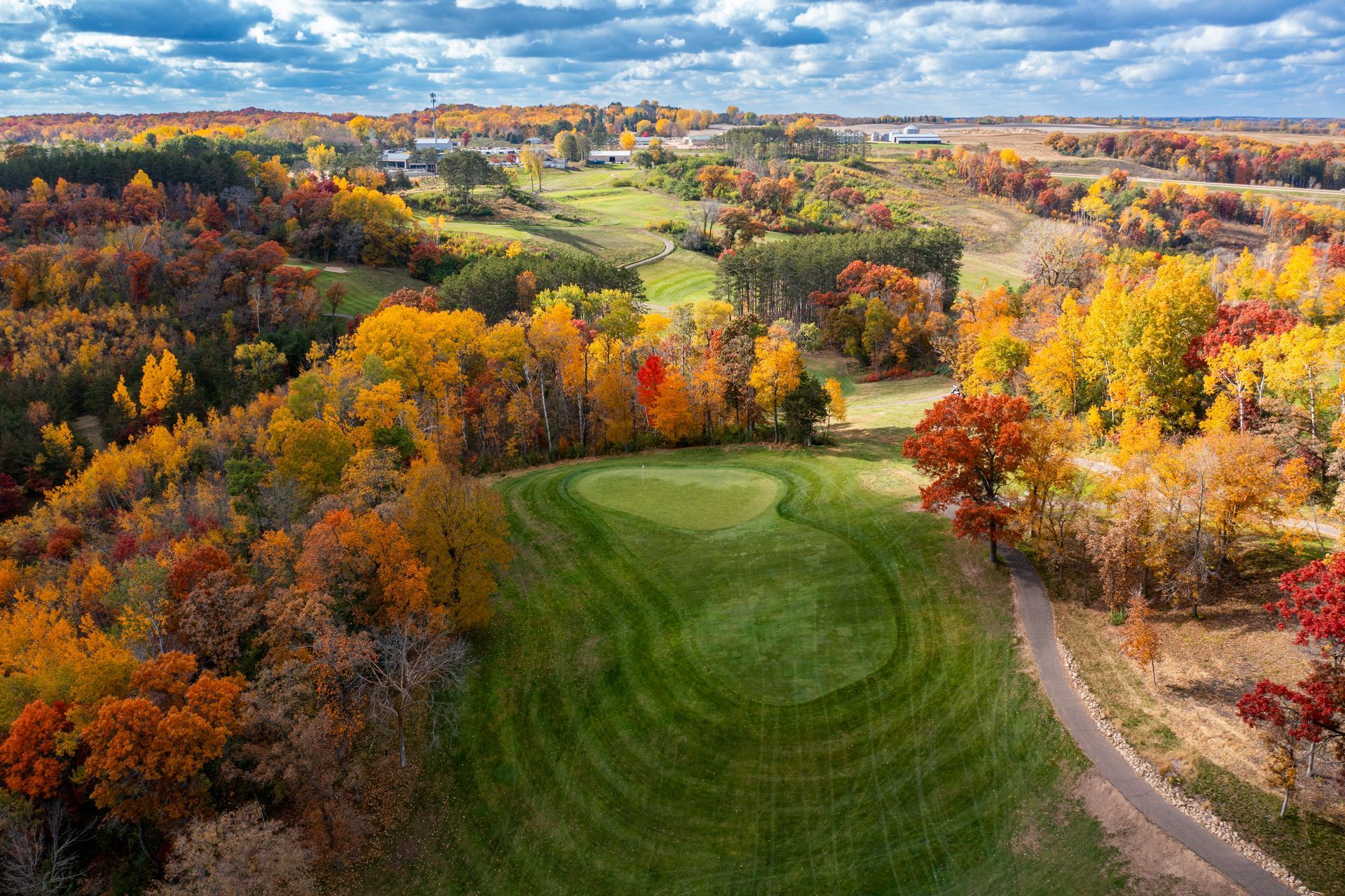 An aerial view of a golf course surrounded by trees in autumn.