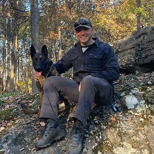 A man is sitting on a rock with a dog in the woods.