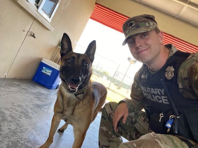 A man wearing a vest that says military police poses with a dog