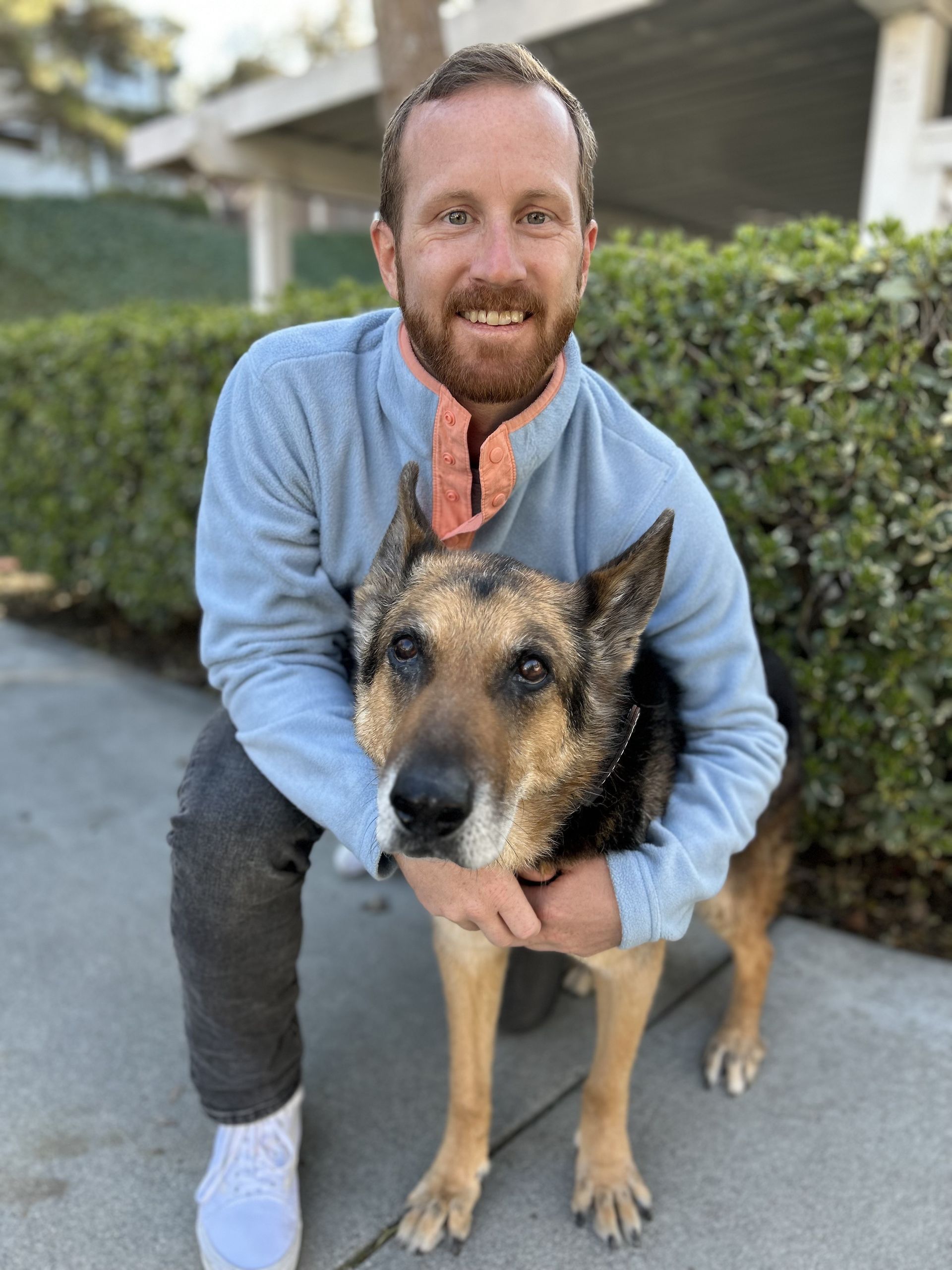 A man is kneeling down next to a dog on a sidewalk.